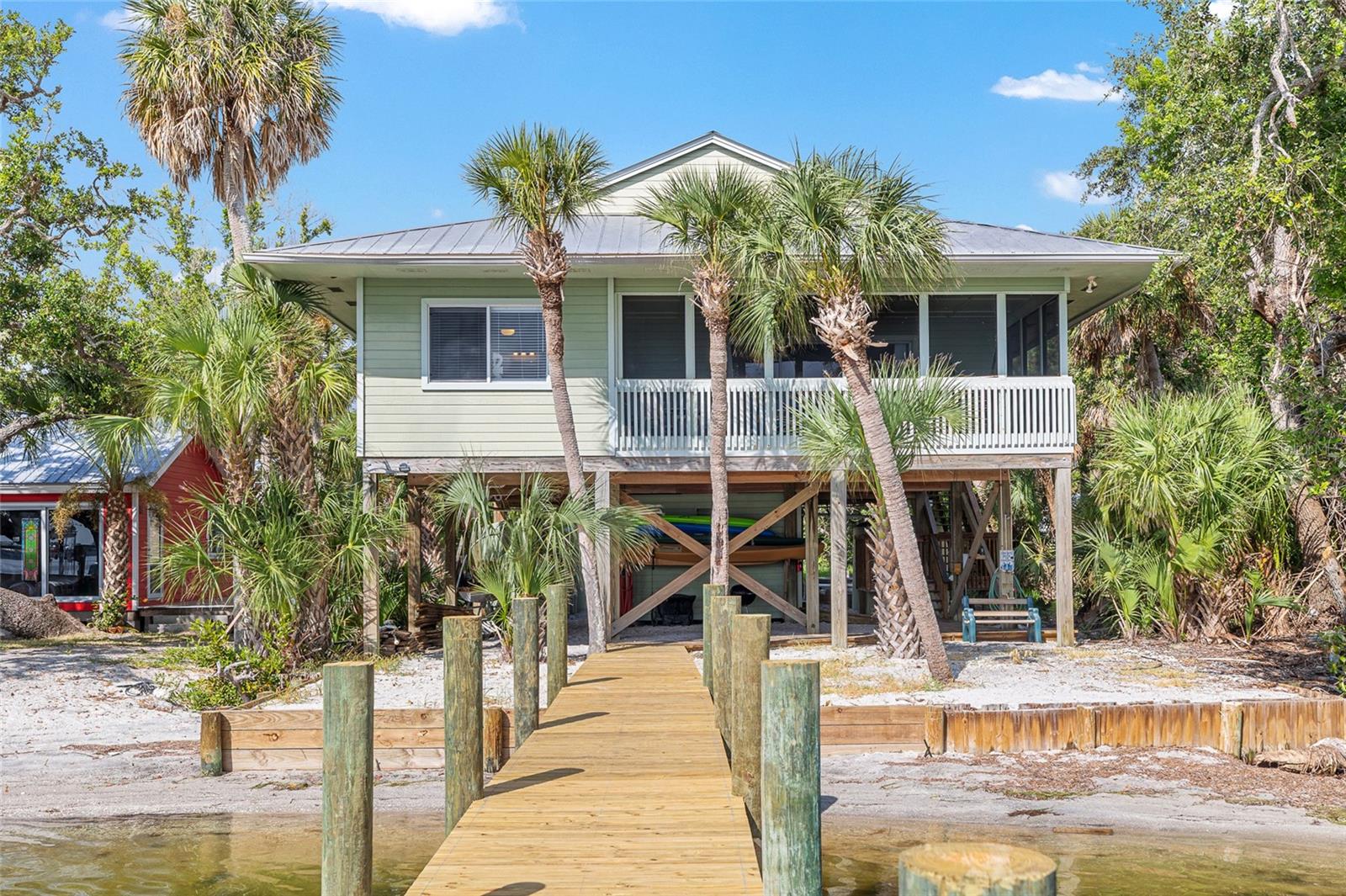 BAYFRONT HOME WITH A PRIVATE DOCK! Escape to your private paradise on Little Gasparilla Island, a bridgeless barrier island just off the Cape Haze Peninsula, accessible only by private boat or water taxi. Free from cars, shops, and crowds, this rare island retreat offers pure tranquility with over 3 miles of pristine, uncrowded beaches for swimming, shelling, shark tooth hunting, fishing, or simply relaxing with a book in the warm gulf breeze. Set on a .37-acre lot stretching 350 feet deep with 50 feet of bayfront (THREE SEPARATE PARCELS INCLUDED IN SALE), this stunning home features a private dock and panoramic views that capture sunrises over the bay and sunsets over the Gulf. Inside, expansive windows flood the open floor plan with natural light, while the chef’s kitchen boasts granite countertops, an extra-long island, and ample storage. Tongue-and-groove wood ceilings in the main living areaadd warmth and character, while the home’s turnkey furnished status makes moving in effortless. With 3 spacious bedrooms, 2 bathrooms, and multiple outdoor living spaces—screened, covered, and open-air—you’ll find endless places to entertain, unwind, and soak in the beauty of dolphins, manatees, and boating activity on the bay.
Practical features make island living easy, including a new metal roof, A/C (2021), outdoor shower, kayak/SUP storage, and an outdoor elevator to carry up groceries and luggage. Storage is abundant for all your beach and boating gear, and sandy golf cart trails let you explore the island and meet welcoming neighbors. Just steps from your door, enjoy beach access to the Gulf’s turquoise waters. Whether you’re searching for a serene family getaway, a vacation rental investment, or your forever island home, this property seamlessly blends comfort, convenience, and the natural beauty of island life.