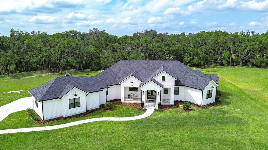 Welcome to the lifestyle you've been waiting for. Set on 5.11 stunning acres, this custom-built Southern Tradition estate is a rare blend of refined elegance, modern luxury, and peaceful, nature-filled surroundings. Whether you crave open space, love to entertain, or simply enjoy the outdoors, this one-of-a-kind property is ready to impress. From the moment you arrive, the white brick front porch and elegant glass French doors welcome you into a home filled with warmth and style. Inside, you'll find 8-foot doorways, soaring ceilings, and rich wood beam accents, all grounded by beautiful wood-look tile flooring that flows throughout the main living areas, including the office and primary suite—offering durability and timeless charm. The kitchen is a true showstopper—straight from the pages of a design magazine. Anchored by a massive center island with quartz countertops, it features top-of-the-line stainless appliances, including a Thermador gas cooktop with electric oven, built-in appliances, custom lighting, and a butler’s pantry that makes entertaining effortless. The great room is equally inviting, with a bold accent wall and pocket sliding doors that open to a sprawling brick-paver lanai—designed for your dream outdoor kitchen and pool. A spacious office sits at the front of the home and features a hidden Murphy door leading directly into the luxurious primary suite—adding both convenience and a touch of intrigue. The suite itself is a private oasis, complete with dual walk-in closets and an ensuite bath that stuns with marble floors, a soaking tub, and a huge walk-in shower with multiple shower heads, including a rainfall feature. The split floor plan offers ultimate privacy, with two additional bedrooms tucked away on the opposite side—one with its own private ensuite and walk-in closet, and the other adjacent to a full bath—ideal for guests or multigenerational living. Additional highlights include a bright dining room overlooking the backyard, a HUGE custom laundry room that combines beauty and functionality, and generous storage throughout the home. Step outside and you’re surrounded by natural beauty—whether you’re enjoying a quiet morning on the front porch, riding your ATVs across your private acreage, or heading out on a walk to the nearby Alafia River. With over 5 acres to explore, the opportunities are endless. And when you’re ready to venture out, you’re just a short drive from it all—close to major highways, Disney, and Florida’s world-famous beaches. Zoned for top-rated schools and just minutes from everyday conveniences, this home delivers luxury living with room to roam—all without sacrificing location.