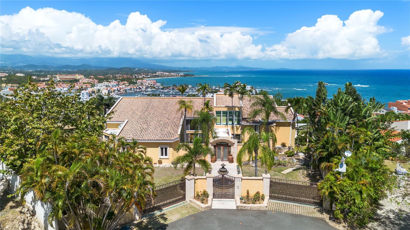 Perched atop the lush, vibrant landscape of Palmas del Mar, this distinguished estate stands in a league of its own, occupying a supremely privileged location that commands sweeping views of the crystalline ocean, majestic mountains, and the sprawling resort below. Designed as an idyllic setting for both grand festive gatherings and tranquil retreat living, the estate's architecture masterfully embraces its surrounding natural beauty through its use of oversized windows, broad terraces, meticulously landscaped garden patios, and an enchanting central courtyard. Upon entering, guests are greeted by a captivating open-air garden, setting the tone for the exquisite interior that lies within.
The interior is a showcase of luxury, featuring rich marble flooring that gleams under the light, intricately designed decorative recessed ceilings, and polished wood accents that add warmth and elegance to the living spaces. These indoor areas are designed to blend seamlessly with the outdoors, ensuring that the beauty of the estate's natural setting is always in view. The master suite serves as a sanctuary of ultimate comfort and luxury, offering an ensuite bathroom equipped with both an invigorating outdoor shower and a soothing jacuzzi, embodying the pinnacle of opulent living. This estate houses five additional bedrooms, each with its unique design and panoramic views of the vibrant outdoor landscape, providing guests with their private retreats. Culinary adventures await in the state-of-the-art kitchen, which boasts dual islands, custom cabinetry, and strategically placed windows that frame the stunning ocean views, inspiring chefs and entertaining hosts alike. The dining room adjacent to the kitchen is designed for hosting lavish dinners, while the estate's variety of outdoor settings offers intimate and versatile spaces for entertaining, including a poolside area with an outdoor kitchen that allows guests to dine al fresco while soaking in the lush resort atmosphere. The estate's Mediterranean-inspired design, characterized by its majestic columns and balustrades set against the backdrop of the garden's vibrant colors, creates a serene yet elegant ambiance, inviting relaxation and enjoyment. With a generous 6,370 square feet of living space and covered parking, this estate grants access to the luxurious amenities of Palmas del Mar, including a tennis center, equestrian center, private schooling options, two championship golf courses, sixteen restaurants and cafes, and the exclusive marina and yacht club, placing it as a rare gem on the east coast of Puerto Rico.
This property holds historical significance as it was originally constructed by Charles Fraser, the original master developer of Palmas del Mar. Among the many available locations, Fraser chose this exceptional spot for his personal residence, marking it as a site of unparalleled value and beauty. Fraser, renowned for his development of iconic destinations such as Kiawah Island, Sea Pines, and Amelia Island, imbued this estate with a legacy of luxury and harmony with nature. As such, this estate does not merely offer a living space but presents a unique opportunity to own a piece of history, offering an unmatched lifestyle in one of the most desirable locations in Puerto Rico.