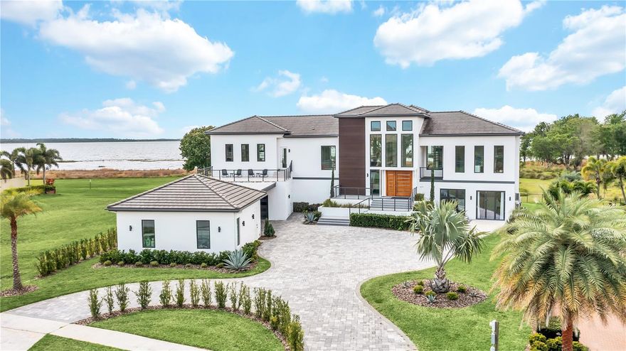 Welcome to 10208 Wittenberg Way, a modern lakefront estate in the private, gated community of Moss Park Reserve. On a 1.52-acre lot with 230 feet of Lake Hart frontage, this custom-designed home offers a blend of mid-century modern inspiration and contemporary villa architecture. Built in 2021, the residence spans over 7,200 square feet and features five spacious bedrooms, five full bathrooms and one half bath. Designed to maximize lake views, the home showcases high ceilings, and large double-paned Low E windows that preview ideal views of the natural surroundings from nearly every room. Notable features include a commercial-grade elevator, gym, billiard/game room, safe room, and three flexible spaces ideal for an office, den or guest suite. Entertain effortlessly with a dramatic entry, expansive indoor-outdoor living and a stunning 40-foot infinity-edge pool that meets lap pool standards. Additional highlights include a four-car garage, and full concrete block construction on both levels.