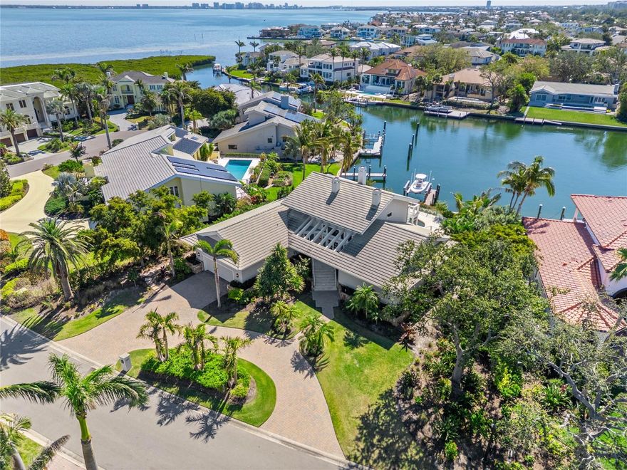 This exquisite two-story waterfront home located in the coveted Harbor section of Bay Isles has been meticulously renovated to embody modern elegance and luxurious coastal living. Surrounded by lush tropical landscaping, the home welcomes you through an elegant French door entrance into the grand foyer, where soaring ceilings, gleaming travertine flooring, and a striking wrought iron floating staircase with rich, dark wood steps set the tone for the refined elegance that unfolds throughout the home. The lower level boasts a bright and airy open space with hardwood floors throughout, creating a welcoming atmosphere that effortlessly combines sophistication with the timeless beauty of natural materials. The spacious family room is anchored by a stunning fireplace with decorative columns and an elegant mantel, complemented by French doors leading to the expansive waterfront lanai, reinforcing the home's seamless connection to its stunning natural surroundings. A culinary enthusiast’s dream, the generously sized kitchen features a large island with a waterfall granite countertop, custom cabinetry, ample storage space, and high-end stainless steel appliances, including a six-burner gas range and double ovens. Adjacent to the kitchen, the dining area and great room spaces flow seamlessly into each other. The great room is both grand and inviting, showcasing a dramatic wood-clad cathedral ceiling that adds warmth and character. A second stone fireplace enhances the ambiance, while three sets of French doors that open onto the lanai offer an effortless transition between indoor and outdoor living. Also on this level are two generous guest suites, each with a full bath, one with direct lanai access, and a den with full bath. Upstairs, the primary suite is a true retreat. Floor-to-ceiling windows illuminate the space, and French doors open to a spacious private balcony, offering captivating water views that create a peaceful escape. A cozy fireplace adds to the intimate atmosphere, while the spa-inspired en-suite bath indulges with marble flooring, soaking tub, dual vanities, frameless glass walk-in shower, and water closet, all overlooking the serene waterway. The outdoor living space is equally spectacular, designed for both relaxation and entertaining. The expansive lanai features multiple covered areas with a rich wood-clad ceiling and retractable screens, a sun-drenched open-air section, and a stunning saltwater pool with travertine decking framed by verdant tropical landscaping. Just beyond the pool, a private dock with a boat lift sits on a deep-water basin and wide canal with no bridges to Sarasota Bay, offering quick and direct access for boating enthusiasts. Bay Isles Beach Club membership is included. This extraordinary home seamlessly blends elegance, comfort, and the unparalleled beauty of waterfront living, creating a sanctuary that is as functional as it is breathtaking.