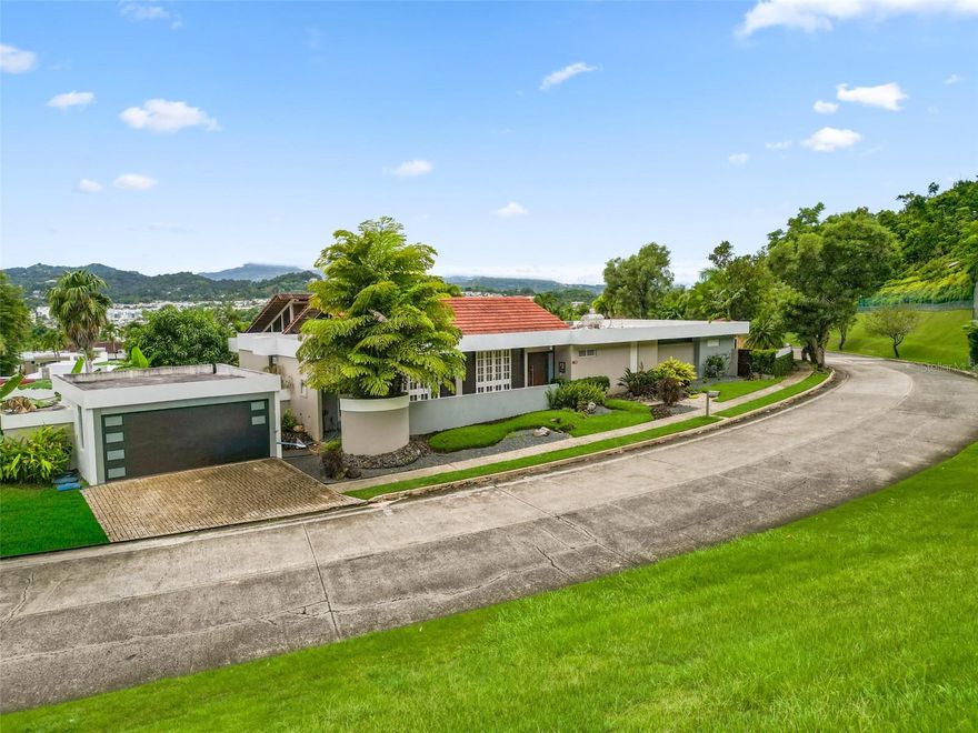 Located in the renowned La Villa de Torrimar community in Guaynabo, this distinctive residence blends architectural elegance with artistic soul. Flooded with natural light, its open layout features vaulted wood ceilings, marble floors, and crystal chandeliers that highlight an exquisite collection of art and design.

The home offers four bedrooms and two and a half bathrooms, along with spacious living, dining, and family areas — perfect for both everyday living and entertaining. Large windows and glass doors seamlessly connect the interior to an expansive terrace surrounded by lush gardens. The outdoor area includes a pool, jacuzzi, and gazebo, creating a serene, resort-like atmosphere.

Set on approximately 960 square meters within a gated community with 24/7 security, this residence embodies a rare balance of sophistication, warmth, and creative energy.
