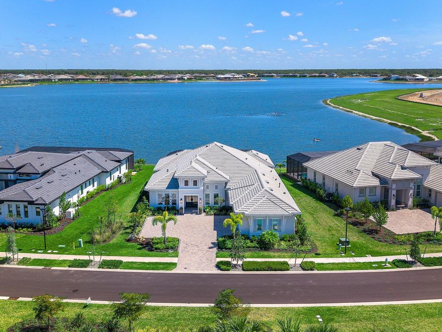 Don't wait for new construction when you can have a pristine, better than new, custom home with mile long water views that is available NOW!  This stunning; lakeside home built in 2024 has been meticulously upgraded post-construction with a multitude of high-end upgrades. Lush landscaping lines the paver driveway, equipped with an oversized parking pad for guests and leads you to the front entry with modern impact full-glass front door.  Inside the foyer you’re immediately greeted with the large lake views that are truly the star of this residence.  Enjoy contemporary design within the open floor plan including both study and bonus room, engineered hardwood flooring, designer light fixtures, volume ceilings with crown molding, plantation shutters, professional custom closets, and a bright light-filled space.  The central great room has a triple tray ceiling, feature wall with built-in cabinetry, and impact sliding glass doors to the lanai with the lake beyond.  The open flow continues into the upgraded kitchen that is expertly outfitted with a central island of waterfall quartz counters, abundant crisp white cabinetry with matte black hardware, glass display cabinets, full-height quartz backsplash, farmhouse sink, walk-in pantry with custom shelving, and top-of-the-line Jenn-Air appliance suite with 6-burner gas cooktop.  Perhaps the most desirable feature of this floor plan is the convenient butler’s wet bar connecting the kitchen to the formal dining room with quartz counters and backsplash, glass display cabinets, and wine refrigerator.  Enjoy elegant occasions in the formal dining room adorned with custom moldings, or casual weeknights in the dinette surrounded by lake views.  But the best place to entertain is on the paver lanai where the lake views take center stage from the covered living area with cozy fireplace, modern ceiling fan, and remote-controlled hurricane screens.  The dining space is highlighted by the custom outdoor kitchen with granite counters, full-height backsplash, stainless steel grill, pizza oven and side burner and beverage refrigerator.  The heated saltwater pool includes a raised spa, water founders, water bowl features and a panoramic screen enclosure framing the lake views. Your primary suite also takes advantage of the remarkable lake views through glass french doors, plus custom triple tray ceiling, dual walk-in closets, and en-suite bath with freestanding tub, oversized walk-in shower, long vanity with dual sinks, and private water closet.  Guests will find their own comfort and privacy in 3 guest bedrooms, all with walk-in closets, 2 of which have private en-suite bathrooms, and the third full bath also works as a pool bath.  Additional spaces include a private study, lakeside bonus room with closet (could be a 5th bedroom), functional laundry room, mudroom entry hall with cabinetry, and impressive 3-car garage with its own air conditioning.  Peace of mind is secured with impact windows and doors, whole-house GENERATOR, and whole-house water filtration.  Wild Blue at Waterside is one of Sarasota’s premier neighborhoods offering upscale amenities including a waterfront clubhouse with restaurant opening fall 2026, dock and kayak launch, 6 tennis courts, 8 pickleball courts, pro shop, outdoor fitness, walking trails, pavilion, playground, dog park, basketball court, and Midway Sports Complex access.  Plus enjoy proximity to Waterside Place with shopping, dining, farmers market, parks, events and more.