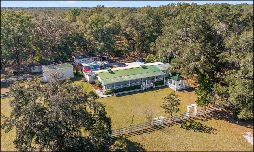 Discover a rare combination of income potential, natural beauty, and peaceful living with this unique and turn-key four-acre property, zoned for horses and perfectly positioned between Ocala and Dunnellon. Just moments from the crystal-clear Rainbow River, you’ll have easy access to kayaking, canoeing, swimming, and tubing. Even more exceptional, the back of the property borders the Cross Florida Greenway and the Pruitt Trailhead, giving you coveted, direct access to miles of horseback-riding and hiking trails, an amenity few properties can offer. The main home provides comfortable everyday living with two bedrooms, two and a half baths, laundry facilities, and an updated AC system in 2021. Multiple back porches, including a screened porch, BBQ area, and a dedicated pool porch, create inviting spaces to relax, entertain, and enjoy tranquil views of the pool and surrounding landscape. A divided pasture with new fencing and upgraded electrical in the workshop and cottages adds to the appeal of this property. Two additional residences add tremendous versatility. The primary guesthouse offers a studio-style layout with one bedroom, one bath, and a kitchenette, all with direct access to the pool deck. A second rental cottage, affectionately known as The Back Porch, features a separate bedroom and living room along with a charming porch overlooking the scenic Greenway. These spaces are ideal for rental income, multigenerational living, or hosting guests in complete comfort. If you prefer to keep the property all to yourself, it easily transforms into a private retreat. Picture quiet mornings on the expansive rocking-chair front porch, taking in serene views of the Greenway and the surrounding natural beauty. The location is exceptional, offering quick access to the World Equestrian Center, the SR 200 corridor, and an array of recreational areas, state parks, and waterways, including Lake Rosseau, the Gulf of Mexico, and the Withlacoochee River. Whether you’re seeking a profitable investment, an equestrian-friendly homestead, or a peaceful sanctuary surrounded by nature, this property delivers a lifestyle filled with comfort, beauty, and endless possibilities.