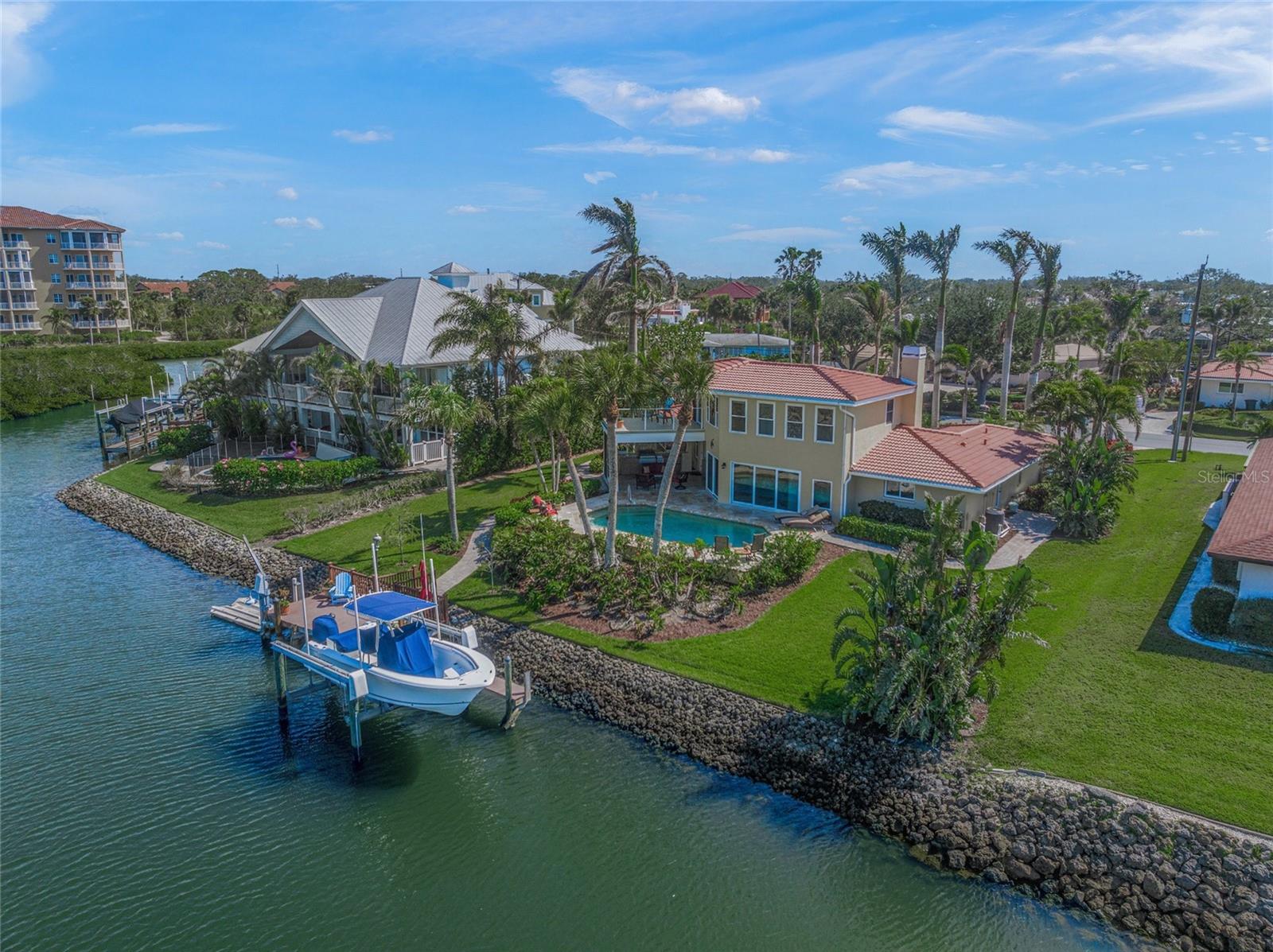 This exquisite waterfront residence offers a dreamlike lifestyle with expansive views of the canal and bay, making it a gem in Sorrento Shores. Boaters dream, 10,000-pound lift in your backyard, 20 minutes to Venice Inlet with access to the turquoise waters of The Gulf. On a prime cul-de-sac lot, the home boasts a stunning circular driveway adorned with majestic Royal Palms, enhancing its curb appeal. As you step inside, you're greeted by breathtaking views that set the tone for tranquil living. The great room, featuring a cozy gas fireplace, serves as the heart of the home, seamlessly connecting to a well-appointed kitchen. This kitchen is a chef's delight, equipped with a center island, granite countertops and stainless steel appliances, all while offering a picturesque view from the sink. The outdoor space is equally impressive, showcasing a large 28-by-15-foot heated pool with a depth of 8 feet, complemented by wraparound decking that invites you to soak in the sublime views. The newly added summer kitchen, complete with cabinetry, a grill, a vented hood, a beverage refrigerator and a sink, creates an ideal setting for alfresco dining and entertaining. The upper-level owner's suite is a private sanctuary, featuring a spacious new composite deck that overlooks the pool area and waterfront. It includes an oversized walk-in closet and a luxurious spa bath, providing a retreat-like experience. Main floor guest bedrooms and baths, with one being en-suite, ensure comfort for visitors. With practical upgrades such as impact windows and doors for peace of mind and a new roof installed in 2024, this home is as functional as it is beautiful. The property spans over one-third of an acre, featuring lush landscaping nourished by an irrigation well. Conveniently near Sarasota and Venice cultural attractions, fine dining, and stunning beaches like Siesta Key and Nokomis Beach, this home offers an enduring lifestyle in harmony with its surroundings. Nationally acclaimed Pine View School is a five-minute drive away. Whether you're observing dolphins and manatees from your deck or enjoying the vibrant local arts scene, this residence embodies the waterfront frame for an exceptional life.