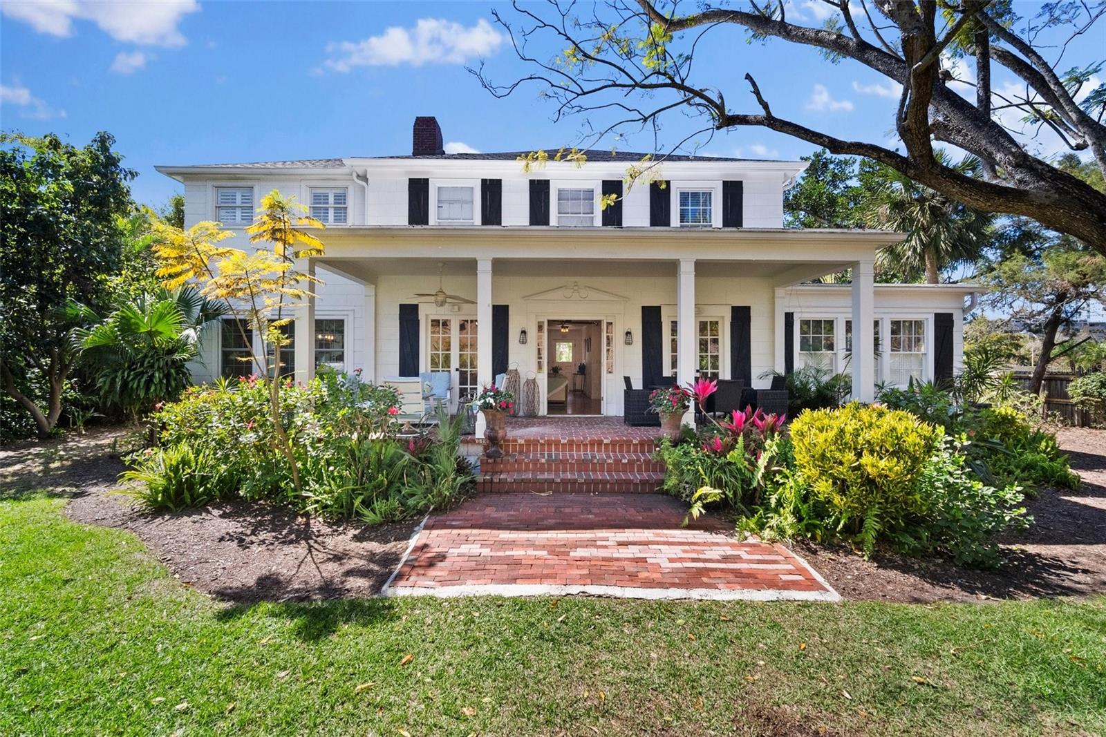 Unique 1936 colonial home in the heart of Sarasota. Located on an expansive corner lot in one of Sarasota’s most desirable neighborhoods, just one block from Selby Gardens and within walking/biking distance to downtown. The main living area features a cozy fireplace and an open flow into the family room, with French doors leading to the first-floor primary suite. The second floor includes two ensuite bedrooms with access to a private guest suite, which has its own entrance, living room, den, and full bath. A ground-floor studio provides the perfect space for an art studio, yoga room, home office, or private retreat. The home offers modern comforts while maintaining its historic charm, with beautiful hardwood floors, an updated kitchen with a dumbwaiter to the second floor, an elevator for convenience, and skylights that fill the space with natural light. Recent upgrades include a new roof in 2024, updated plumbing and electrical, and three separate A/C zones. The oversized garage includes workshop space, and the expansive lot provides room for a pool or additional landscaping. While the home carries a rich history, it is not designated historic, allowing for future customization. Bayfront Park is only steps away, offering stunning sunset views over the John Ringling Bridge. Originally built in 1936 and relocated across the street in the 1980s, the home was placed on a raised cement block foundation to meet flood guidelines while preserving its architectural character. A significant second-floor addition was completed in 2003 and expanded the home to over 4,000 square feet, adding additional living areas, a bathroom, an atelier with skylights, and bringing the total to five bedrooms and four bathrooms. This unique property blends character, space, and an unbeatable location.