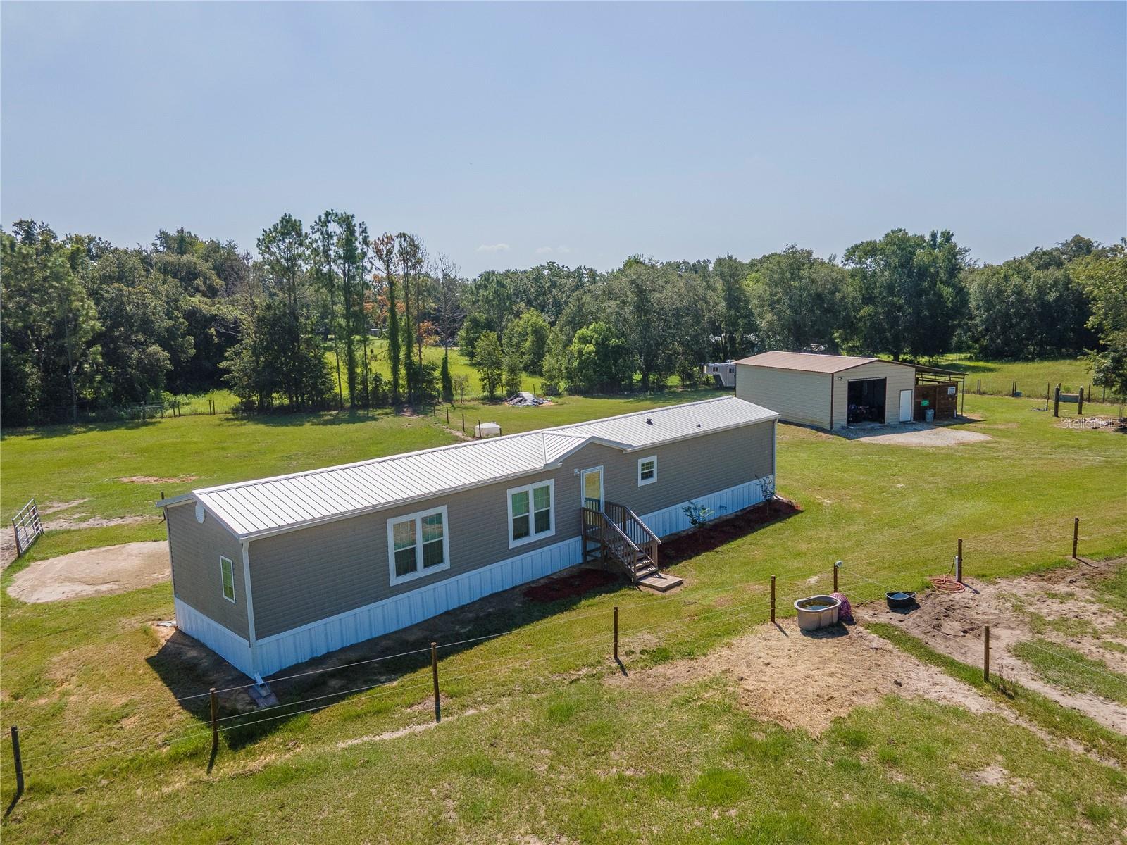 Looking for wide open space with no HOA, no CDD, and room for your animals, toys, and hobbies? This 2024-built, move-in-ready 2-bedroom, 2-bath mobile home on 2.4 acres has it all — and more!
Set on fully fenced and cross-fenced agricultural-zoned land, this 1,140 sq ft home features a split-bedroom layout perfect for privacy. The secondary bedroom and full bath are conveniently located off the entrance, ideal for guests or family. As you step into the open-concept living area, you'll be greeted by beautiful wood plank laminate flooring throughout (with cozy carpet in the bedrooms), a decorative accent wall with built-in electric fireplace, and a stylish kitchen with stainless steel appliances, abundant cabinetry, and designer finishes — perfect for both everyday living and entertaining.
The spacious primary suite includes an upgraded en-suite bath, offering a private retreat at the end of the day.
Outside, this property is fully equipped for your rural lifestyle. A 10x24 lean-to in the pasture provides shelter for animals, and the 22x35 insulated workshop features underground electric and a 100-amp panel — great for hobbies, projects, or storage. The property also includes three 12x11 horse stalls and camper hookups: two 30-amp and one 50-amp service connections.
While you'll enjoy the peace and quiet of country living, you're just 2 miles from conveniences like Walmart, Lowe’s, Publix, Tractor Supply, Rural King, restaurants, entertainment, and more.
This is the rare blend of rural charm and modern comfort — don’t miss your chance to call it home. Schedule your private tour today!