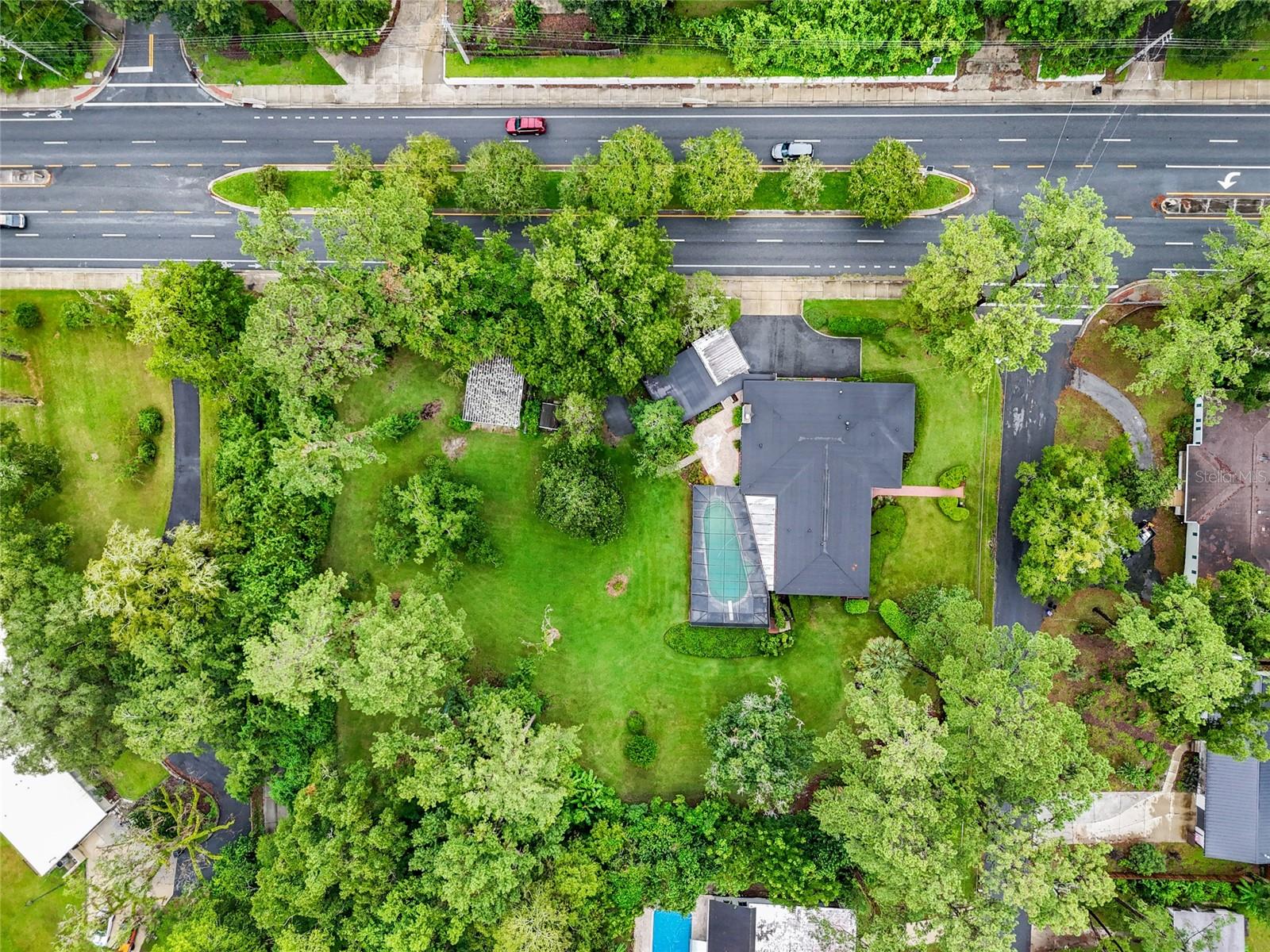 Tucked away on a lush, nearly half-acre parcel in the coveted Mason Manor neighborhood, this timeless 1957 pool home offers approximately 3,425 sq ft of living space, all on one level of solid concrete block construction. With 4 bedrooms, 3.5 baths, warm hardwood floors, and a stately brick fireplace, it’s a home that feels both rooted in history and ready for new stories.
Your tour begins in a sunlit foyer, where gleaming original hardwoods and twin coat closets welcome you in. Down the left wing, three tranquil bedrooms await, two with views of the sparkling pool and their own doors to the deck. A guest bath offers a second exterior entrance, perfect for poolside gatherings. At the far end, the primary suite unfolds like a private sanctuary, with an expansive ensuite bath and a walk-in closet the size of a small room.
At the heart of the home, the kitchen is a picture of classic craftsmanship, featuring solid wood cabinetry, a charming farmhouse tile backsplash, and a peninsular island for casual dining or conversation. Windows wrap the space in natural light, offering serene views of the pool and lush backyard. The breakfast nook’s French doors lead straight to the shaded patio and pool deck. A formal dining room flows seamlessly into an intimate sitting area, then onward to the grand 20’ x 33’ family room complete with a brick fireplace, custom wood built-ins, and a cozy bay window seat.
A private fourth bedroom suite rests just beyond, separated by the laundry room and a spacious utility area, ideal for guests, extended family, or a quiet work-from-home haven.
Outside, a storybook setting unfolds: a charming courtyard, a sweep of emerald lawn, and a massive covered patio beneath your caged pool deck. The north-side driveway offers parking for up to four vehicles in addition to an oversized two-car garage. Daily walks to Loblolly Woods Nature Park and Hogtown Creek are just steps away, with a trail entrance down the street. Summer afternoons and starlit evenings have never looked better. The two adjacent lots are being offered separately, but all three parcels can be purchased together to create a rare estate property in the heart of Gainesville.