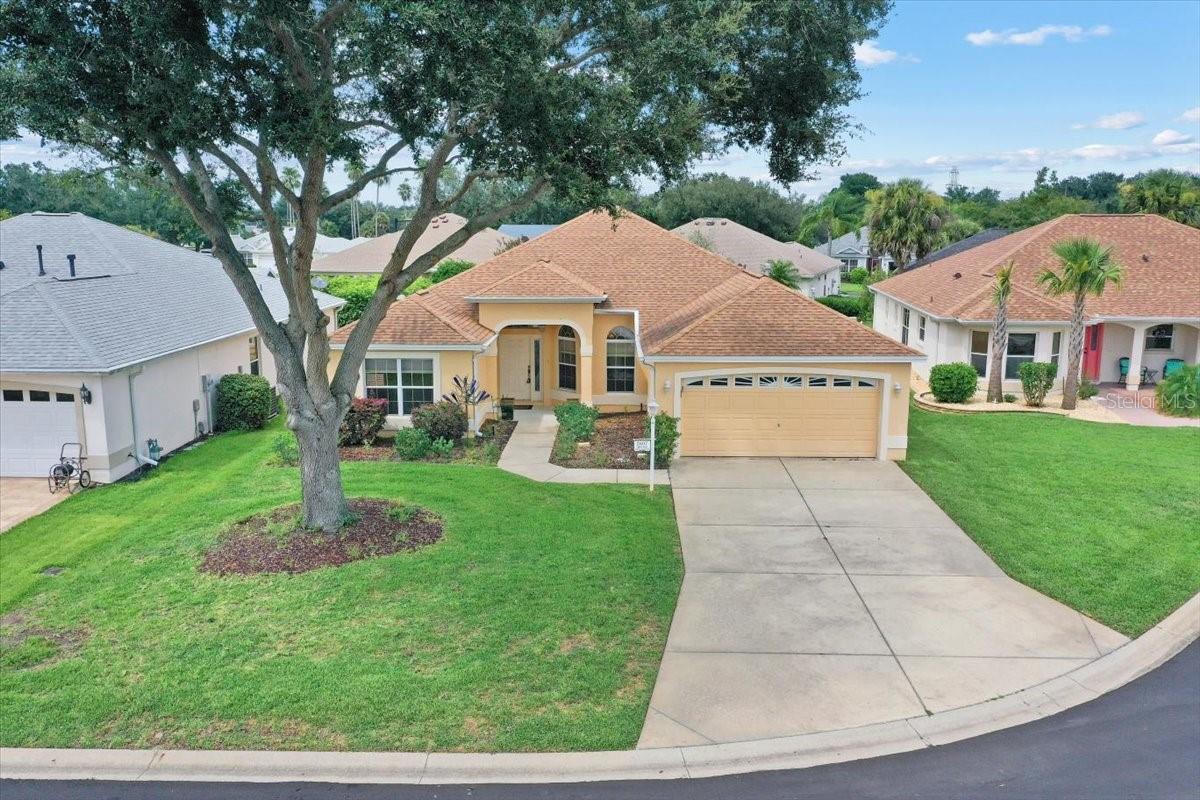NO BOND! Welcome to this Volusia model located in The Village of Santiago. Upon arriving at this beautiful home, the expansive driveway and beautifully manicured tree greet you. Upon entering through the front door, a hallway to the left guides you to two spacious bedrooms and a guest bathroom featuring a tiled tub/shower combo. The oversized owner's suite, situated on the opposite side of the home, has been partitioned to create an additional flexible space for your needs. A hallway leads to two separate closets, one equipped with built-ins, and an owner's suite that includes dual sinks, a walk-in tiled shower with a stool, and a linen closet. The bright, open kitchen features an eat-at bar, a nook area, recessed lighting, and ample storage space. You can appreciate the hardwood floors, as you transition into the dining room and living area. The living room boasts two large windows that allow natural light, a fan/light combo, and a floor plug for convenience. This space seamlessly flows into the enclosed lanai, which includes three transom windows and three large glass doors with shades, as well as tiled floors. The indoor laundry room is equipped with a washer, dryer, cabinets, and an additional refrigerator. Furthermore, the 18'5" x 30" garage provides an excellent space. ROOF & AC replaced in 2019. The property’s excellent location provides convenient access to all your needs, including the nearby recreational Center, shopping, dining, medical offices, and entertainment at Sumter Landing and Brownwood squares—all just minutes away. Don’t miss the opportunity to own this remarkable home in THE VILLAGES—schedule your tour today!