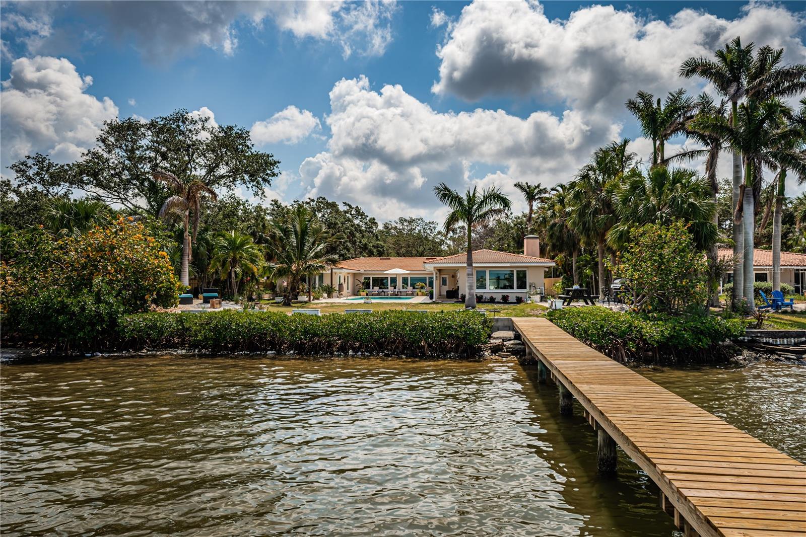 Discover the essence of waterfront luxury in the coveted Jungle Terrace neighborhood. Nestled on a tranquil dead-end street, this rare gem offers unparalleled privacy and breathtaking views of Boca Ciega Bay. Sitting on nearly half an acre of lush tropical landscaping, this serene retreat invites you to embrace coastal living at its finest. Watch dolphins, manatees, and exotic birds as they glide through the waters near the protected sanctuary of Dog Leg Key—an oasis of natural beauty and relaxation.
An entertainer’s dream, this waterfront haven offers the ultimate in outdoor living. The backyard is designed for relaxation and fun, featuring a sparkling saltwater pool and a spacious patio—partially covered to ensure year-round enjoyment. A charming, landscaped picnic area guides you to the newly refurbished dock, complete with a permitted lift (not operable), offering seamless access to Boca Ciega Bay for boating and water activities. Lush greenery thrives with the help of a well-fed irrigation system, creating a vibrant coastal retreat. Adding to the privacy and exclusivity, the property benefits from a 40-ft-wide neighborhood water access along the north property line, ensuring peaceful separation from neighboring homes.
A circular driveway leads to the front entrance, offering ample parking in addition to an attached two-car garage. The moment you step inside, large windows frame the serene bay views, immediately immersing you in the beauty of the surroundings. The open floor plan creates seamless flow between living and dining areas, providing plenty of space for entertaining or quiet relaxation. The spacious kitchen offers easy access to the rest of the home, making it ideal for hosting guests.
On one side of the home, the primary bedroom suite features a large en-suite bathroom complete with a private sauna. On the opposite side, two additional bedrooms, each with their own en-suite bathrooms, provide comfort and privacy. Separated by a breezeway, the 700 sq. ft. guest suite provides a versatile living space with a wood-burning fireplace, kitchenette, full bathroom, and sleeping area. This unique feature can serve as an income property, pool house, game room, or guest retreat.
Additional property features include travertine flooring, newer low E thermal pane windows (2016), new kitchen appliances (refrigerator, range and dishwasher in 2025), elevated HVAC (2025) systems and water(2025) heaters, new main electrical panel and sub panels (2025), newer water softener/filtration system (2022) and updated pool equipment (2025) for effortless maintenance.
The property was professionally remediated following recent hurricanes, and a transferable flood insurance policy through the National Flood Insurance Program ensures added peace of mind. Some of the improvements post hurricane include fiberglass wall insulation replaced with rigid board insulation and drywall replaced with cement board or stucco in most areas. For more information, take a look at the documentation in the attachments.
Whether you're relaxing poolside, enjoying vibrant sunsets, or exploring the nearby award-winning beaches and downtown St. Petersburg, this home offers endless possibilities for luxury waterfront living.