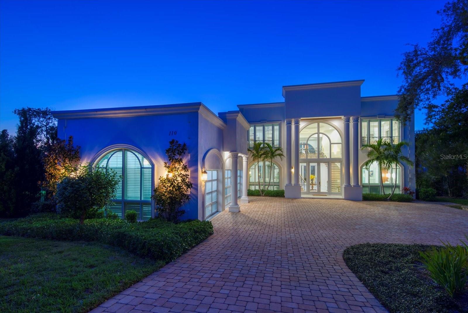 Experience modern luxury in this contemporary estate perched atop a bluff, standing 35+ feet high above base elevation on a sprawling 1+ acre lot with breathtaking views of the intracoastal waterway. Upon entering the grand foyer, you’re greeted by an impressive double staircase and soaring 20+ foot ceilings that seamlessly lead into an expansive living room framed by floor-to-ceiling windows. Elegant pearl marble flooring flows throughout the home, while the bedrooms showcase rich hardwood floors. Expansive glass doors and generous windows capture picture-perfect sunsets year-round. This residence boasts an array of upscale features including professional-grade appliances from Wolf, Sub Zero, and Bosch, two luxurious linear fireplaces, a recessed LED lighting system, and a private elevator. The massive chef's kitchen features onyx countertop, white cabinetry, pot filler, dual dishwasher, gas range and is a great place to entertain. The first floor primary suite offers stunning views, a linear fireplace and dual walk-in closets. The primary bath features a glass enclosed shower, dual floating vanity and soaking tub. The additional bedrooms and loft are up the grand staircase and have high ceilings, custom moldings, walk in closets. Enjoy the convenience of full laundry facilities on both floors and custom outfitted closet systems. Additional highlights include a spacious three-car garage, refined natural stone accents, temperature-controlled wine coolers, a loft, formal living and dining areas, and an outdoor marble terrace. Day or night, relax outside and enjoy stunning views and indulge in a resort-style infinity pool/spa with tiled fire bowls. With over 100 feet of water frontage and a composite boat dock with 15K lb. lift, there is deep water and easy access to the Gulf. This exceptional location, elevated setting, and premium construction makes this one-of-a-kind estate an absolute must-see.