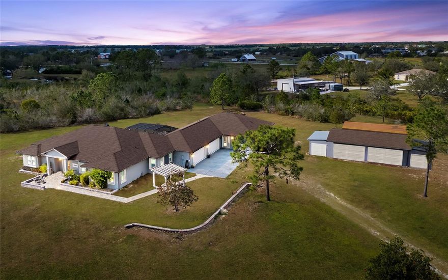 Privacy. Fresh air. Peace and quiet. Come live a country lifestyle with plenty of room to roam inside and out! Farm animals, poultry, food gardens and wildlife watching are welcome here. At night you can look up and gaze at the brilliance of the star-lit sky. In Myakka City, this 7.3-acre property offers a secluded location just 20 minutes from in-town amenities at Lakewood Ranch and the Interstate 75/SR 70 interchange. This country compound ticks all the boxes. main house with four bedrooms and three baths, separate guest house with two bedrooms and two baths, four-car attached garage, six-car detached garage, oversize carport, well pump shed and freshwater pond. Offering 4,808 square feet of combined living space, the flexible floor plan can be configured to your heart’s desire. Luxury features include engineered hardwood floor in living areas, crown molding, solid wood cabinetry, impact glass windows and doors, built-in fire pit and newer roof in 2020. Both houses are fully independent with separate entrances, kitchens, laundries and covered lanais. They share a screened-in swimming pool and outdoor patio with wood-burning fire pit. The detached 1,000-square-foot, four-car garage has two attached single garages and creates unlimited possibilities for pursuit of hobbies, family life and homesteading. Nature lovers can experience the real Florida in two nearby state parks. Nature walks, bird watching, kayaking and overnight camping are available at Lake Manatee State Park and Myakka River State Park. For those who thrive on outdoor challenges, TreeUmph! Adventure Course for climbing and swinging through the trees is just seven minutes away. In all, come home to an incredible place to live, approved by Mother Nature.