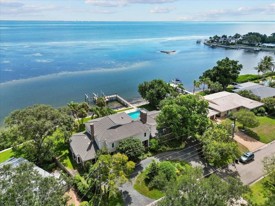 Stunning Panoramic 147 feet of WATERFRONT views, a large private boat dock with TWO boat lifts, and a private POOL located on the peak of the bay kissing the water that didn't have any water intrusion or damages during the record-breaking hurricanes in 2024? You're not dreaming. It’s REAL. This spacious plantation-style home is the perfect blend of Old Florida character and modern luxury. Tucked away on a large private lot on the peak of the curved bay, this magnificent property is surrounded by a variety of views, fruit trees, exotic plants, and tropical wildlife. With almost every room having a beautiful view of the sparkling water, you’ll never forget why you chose this as the place to call home. You'll immediately be greeted by water views through the grand entryway into the dining room as you move past the beautiful cantilever staircase wrapping up to the second floor. The endless water views from the open kitchen and living area are breathtaking. Talk about a perfect place to entertain! The spacious open living/kitchen area features an enormous kitchen with island, built-in Sub-Zero refrigerator, Elise range and gorgeous unique countertops, large bar with separate sink, unique, rare, and authentic Florida Keystone coral rock fireplace, and impact sliding glass doors out to the back lanai, making indoor/outdoor entertaining a breeze. Words cannot describe the views from outside. Whether you want to swim in the private pool, have dinner on the lanai, watch the wildlife with your coffee, or hop on the boat from your dock with not one, but TWO boat lifts…this home has you covered…and a view of the water from almost every angle. There is space for all of your toys on this expansive dock and room for all your outdoor activities in the large yard along the water. 
This home features a library with floor to ceiling solid wood shelving and a fireplace that is like something out of a fairy tale! If the library isn't cozy enough, there's a total of THREE fireplaces throughout the home. With 5 bedrooms and 5 and a half bathrooms, you’ll have enough space for everyone. There’s even a bonus room with a view that would make working from home, exercising, or whatever you want to do in there seem like you're still on vacation somewhere! The covered balcony of the second floor runs the length of the home, giving the bedrooms along the back not only a view from their window, but a place to step outside and FEEL the bay breeze. This home was designed to enjoy the views as both stories have an outdoor space that runs the entire length. 
The FIRST FLOOR BEDROOM has an exterior door leading out to the back lanai and is large enough to be an in-law suite, a second primary bedroom, or transformed into a game room. The sky is the limit for this unique space.
Impact windows throughout, slate tile roof, new pool heater/chiller, luxury appliances, wet bar with wine fridge, ice maker, and liquor cabinet with lock, 15 minutes to The Don Cesar and Gulf Beaches, 12 minutes to all the action of downtown St. Petersburg, 30 minutes from Tampa, and 45 minutes from Sarasota…you will NOT find a better location. Be close to everything, but far enough to be in your own world. Properties like this are RARE. Waterfront properties that encountered ZERO damages during last year's hurricanes are RARE. Private docks with TWO boat lifts are RARE. If you were waiting for the perfect pool home on the open water with a dock with not one, but TWO boat lifts, THIS. IS. IT.