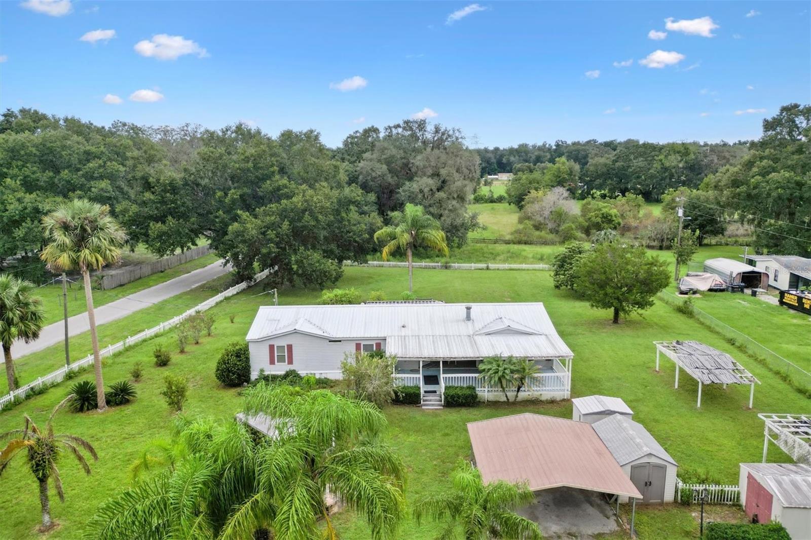 Your own PRIVATE OASIS where country dreams come true! Ready to escape the hustle and create your perfect life? This spacious manufactured home on 2.4 ACRES offers pure freedom with NO HOA, no rules, just YOU living your best life with all your furry and feathered family members. This hidden gem feels like you're miles from everything, yet you're minutes from all the conveniences you need. The home is original and ready for your personal touch, priced to sell and perfect for someone with vision and handy skills. Step onto the welcoming 30+ft covered deck and into the unique oversized foyer with room for all your gear. The open-concept living flows beautifully between the spacious living room with wood burning fireplace and defined dining area, all wrapping around a massive kitchen with double pantry cabinets and pass-through bar perfect for entertaining. The attached laundry room provides direct access to the open deck where you can soak in the view of your property. The split bedroom layout offers maximum privacy with a primary suite featuring dual walk-in closets and spa-like bathroom with double sinks, large soaking tub, and separate shower. Two additional well-sized bedrooms with ample closet space share a full guest bath. Solar tubes enhance interior lighting and all of the windows are vinyl double pane for increased efficiency. Zoning allows up to 3 hooved animals (AUEs) and 10 fowl per acre (not including the home). The property is already fenced and cross-fenced with multiple storage sheds, animal shade structures, pergola, and 2-car carport. The CORNER LOT bonus means direct road access to your back acre for ultimate convenience. A covered screen room extends your living space while you enjoy those peaceful pasture views. No through traffic means true privacy and quiet, yet shopping, dining, medical care, and entertainment are all nearby, plus the new Villages Charter High School is just 7.5 miles away. This isn't just a house, IT’S YOUR CHANCE TO BUILD THE LIFESYLE YOU’VE ALWAYS WANTED with peace, quiet, and endless possibilities. Ready to make it yours?