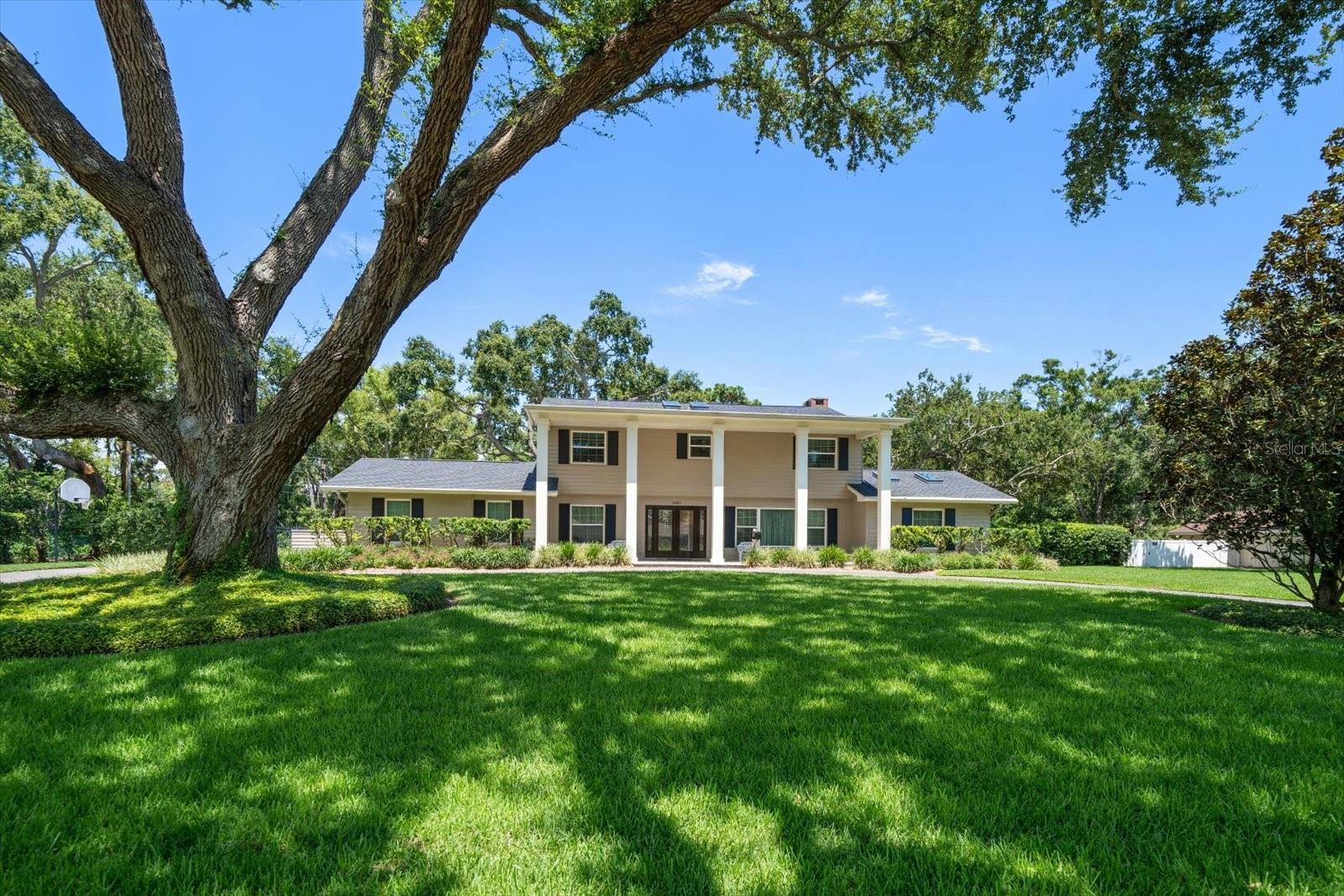 Quietly tucked away on one of Clearwater’s most desirable streets, this stately home offers the perfect blend of timeless elegance, peaceful privacy, and unbeatable location. From the moment you arrive, the curb appeal is undeniable—with a circular driveway, grand columns, and a welcoming front porch inviting you in. Beautiful double leaded glass doors open to a traditional floor plan that feels both refined and relaxed. The spacious dining room is ideal for hosting, while the stunning two-level living room—complete with skylights—sets the stage for entertaining, reading, or simply enjoying your favorite music. Anchoring the warm and inviting family room is a gorgeous wood-burning fireplace, highlighted by recessed and cove lighting and rich custom beams. French doors lead to an expansive screened patio with ceiling fans and overhead lighting, overlooking the beautifully landscaped backyard—completely fenced for privacy, with plenty of space for tennis, pickleball, or simply soaking in the serenity. The chef’s kitchen is sparkling white and outfitted with granite counters, a large island, top-of-the-line stainless steel appliances including a double oven with convection, Bosch dishwasher, and Jenn-Air cooktop, as well as a custom backsplash and sliders leading directly to the pool—perfect for indoor-outdoor entertaining. A convenient and half bath features a wood vanity with marble countertops. The primary suite is a private retreat with gorgeous crown molding, custom cove lighting, French doors to the patio, dual closets including a walk-in with custom built-ins, and a luxurious ensuite bath with double vanities, a jetted tub, and a large glass walk-in shower. Upstairs, two sets of generously sized bedrooms share Jack and Jill baths with double vanities, offering comfort and privacy for family and guests. The larger upstairs bedroom is perfect for guests seeking an extended stay. The oversized laundry room and garage with epoxy floors and a separate storage room provide all the functionality you need. Additional features include hurricane-rated windows and doors, a 2018 roof, smart AC, whole-house generator, smart water shutoff valve, two hot water heaters, full sprinkler system, and more. This is country-like living just minutes from top-rated restaurants, shopping, airports, and world-famous beaches—privacy and luxury in the heart of the city. Homes like this rarely become available—don’t miss your chance to own this one-of-a-kind Clearwater retreat.