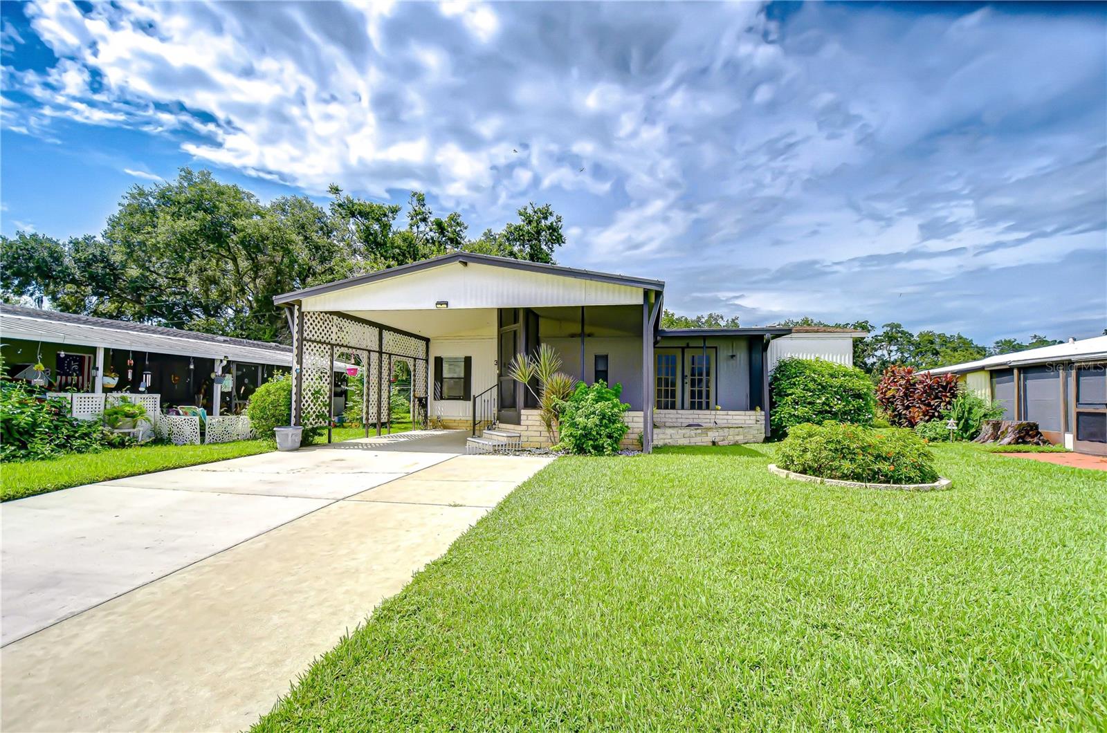 Welcome to Timber Lake Estates — a gated, community offering great amenities and a convenient location! This spacious 2-bedroom, 2-bath home features a covered carport, extra concrete pad to give more parking space in driveway, screened front porch, and a private rear courtyard complete with two storage sheds. Inside, you'll find a large living room that flows seamlessly into the dining area, highlighted by a built-in China cabinet/ buffet. The kitchen offers a breakfast bar perfect for casual meals. The primary suite includes a walk-in closet and a private bathroom with a shower. No age restriction & No lot rent. Enjoy access to two clubhouses, two pools, and community activities and low monthly fee that covers lawn maintenance, water, sewer, and trash. Located near Home Depot, Publix, restaurants, gym, and Wiregrass Town Center, with easy access to Tampa.