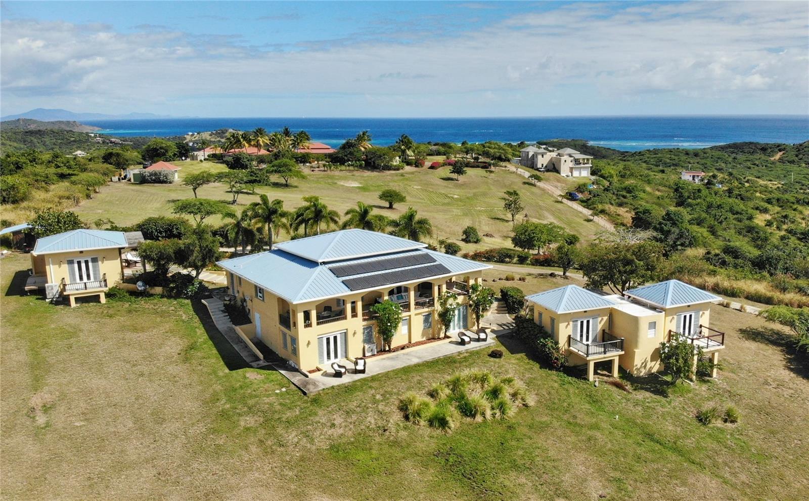This extraordinary 5 acre property celebrate coastal living with its three-building layout, showcasing the timeless elegance of Caribbean architecture with its soaring high ceilings and distinctive 4-pitch roofs. The generous main structure anchors the compound with its thoughtful two-level design. The upper level flows effortlessly from the kitchen through an elegant light-filled living room, where glass doors surround the structure, perfectly framing the island's vibrant tropical colors while inviting refreshing cross breezes to flow naturally throughout the home. On the lower level, two bedrooms Jack-and-Jill style, provide comfortable accommodations with shared convenience and privacy. The magnificent main porch offers ample space for large gatherings and dining alfresco, while intimate bedroom porches create perfect settings for romantic sunsets and quiet contemplation. The dedicated master suite structure provides ultimate privacy, where you can wake up to ocean views right from your bed. The third structure houses two additional bedrooms, each opening onto private porches that offers intimate spaces for morning coffee or evening relaxation so your visitors will enjoy the perfect balance of comfort and privacy.
