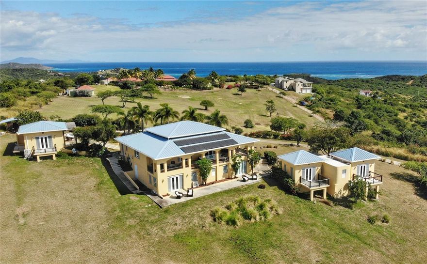 This extraordinary 5 acre property celebrate coastal living with its three-building layout, showcasing the timeless elegance of Caribbean architecture with its soaring high ceilings and distinctive 4-pitch roofs. The generous main structure anchors the compound with its thoughtful two-level design. The upper level flows effortlessly from the kitchen through an elegant light-filled living room, where glass doors surround the structure, perfectly framing the island's vibrant tropical colors while inviting refreshing cross breezes to flow naturally throughout the home. On the lower level, two bedrooms Jack-and-Jill style, provide comfortable accommodations with shared convenience and privacy. The magnificent main porch offers ample space for large gatherings and dining alfresco, while intimate bedroom porches create perfect settings for romantic sunsets and quiet contemplation.  The dedicated master suite structure provides ultimate privacy, where you can wake up to ocean views right from your bed. The third structure houses two additional bedrooms, each opening onto private porches that offers intimate spaces for morning coffee or evening relaxation so your visitors will enjoy the perfect balance of comfort and privacy.
