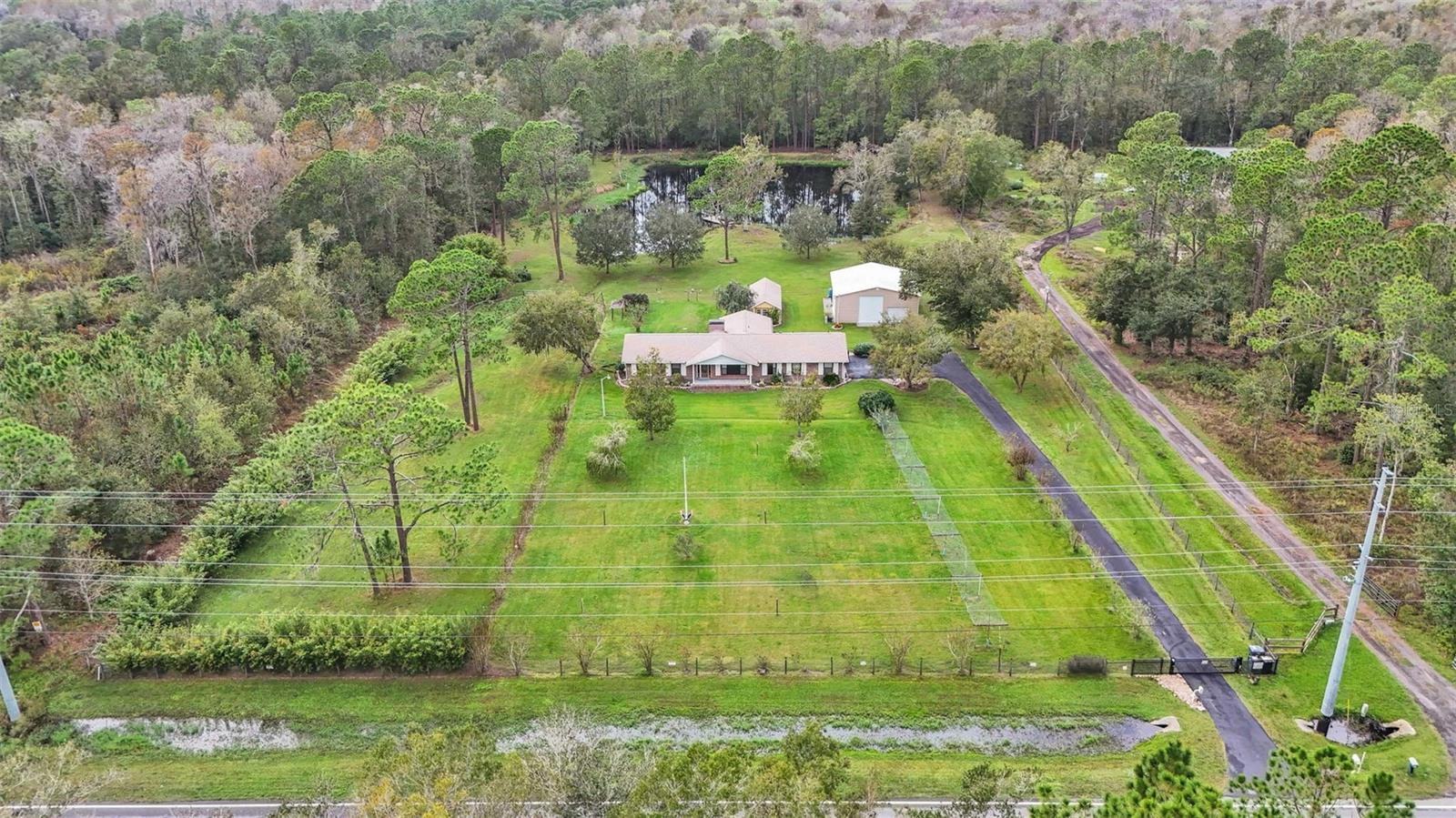 Discover country living at its finest with this stunning 3-bedroom, 2-bathroom home set on 4 serene acres in Lakeland, Florida—where elegant living meets peaceful country charm. Surrounded by mature trees and lush landscaping, the property features a fully stocked private pond with a dock, abundant wildlife, and breathtaking sunset views—complete with a small boat for leisurely fishing. Inside, the meticulously remodeled block-built home boasts engineered hardwood and tile flooring, energy-efficient windows, and hurricane ready plantation shutters. The chef’s kitchen shines with solid wood cabinetry, pull-out storage, a center island, and premium appliances including a GE Café range and LG refrigerator. Enjoy the cozy wood-burning fireplace in the great room, formal dining, and a sun-filled Florida room with its own mini-split AC overlooking the pond. The spacious primary suite includes dual closets and sits next to the main bathroom with a tiled walk-in shower, dual sinks, and under-cabinet lighting. The second bathroom features matching high-end finishes. Major upgrades include a 2022 roof, a high-efficiency Trane 19 SEER AC with heat pump, On-demand tankless hot water heater, updated fixtures, and ceiling fans. Outdoors, a 36' x 36' hurricane ready steel workshop on a concrete slab provides space for RVs, boats, or hobbies, while a block-built garden shed, separate fenced pasture for livestock, and even a private gun range area adds incredible versatility. The wire electric fence with gated entry, asphalt driveway, and ample parking ensure both security and convenience. Located just minutes from I-4, shopping, dining, and a brand-new county fire station, this one-of-a-kind retreat blends rural privacy with easy access to modern amenities—schedule your private tour today!