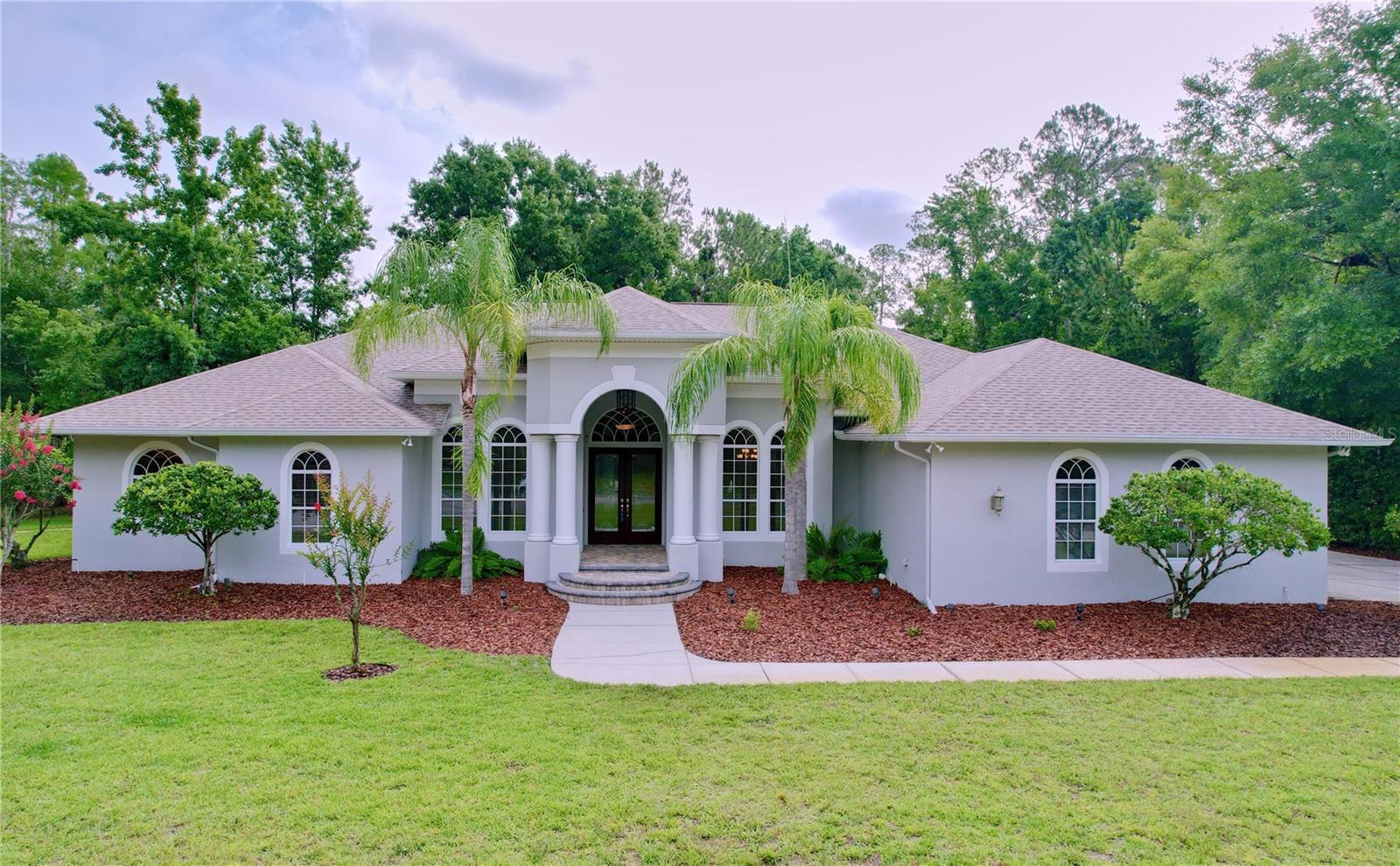 CUSTOM BUILT HOME on 1.5 Acres in a GATED EQUESTRIAN COMMUNITY. This luxurious 5 Bedroom, 4 Bath has an Office, Game Room, Media Room plus 6 Garage Spaces! Great Location just off I-75 in Wesley Chapel, Saddlewood is a serene Enclave of custom built Estate Homes With lots of trees & wooded areas, you’ll see deer, turkeys, migratory birds and neighbors on horses. This Single Story Home has a Unique 3-Way Split Floor Plan that invites Multi-Generational Families with 2 Primary Suites on separate sides of the home that both offer Full Baths & Walk-In Closets. With 4200 Sq. Ft. of Living Area, the rooms are LARGE & inviting with high end finishes & top-of-the-line upgrades. As you walk up to the home, you’ll notice that there are 2 driveways. The first leads to the oversized side entry 2 Car Garage with large access door and then the second driveway on the left side of the property leads to a separate 3 CAR GARAGE/WORKSHOP but don’t miss the Golf Cart Garage at the back of the home that is great for Storage. With 6 Total Garage Spaces & 2 Driveways, you’ll have plenty of parking available! Beginning at the entry, you’ll see the semi-circular front entry stairs leading up and through the Custom Front Doors into the foyer. Custom tile insets, Columns, Archways, Art Niches, Tray Ceiling, 8 Ft. Doors and Dramatically Ascending Ceiling Heights ranging from 10, 12 to 14 Feet demonstrate how well thought out this homes design is. The Views from the Living Room, Kitchen & Primary Suite are all Stunning Wooded Views. The Formal Living Room has Triple Pocketing Sliding Doors out to the fully screened PAVER Lanai. The Chef's Kitchen features stunning custom marble counters & backsplash, euro-style wood cabinets designed with easily accessible drawers. Upgraded Kitchen Appliances include: Monogram Advantium & Trivection Speed-Cook ovens, Wolf five-burner glass cooktop, Monogram warming drawer, 48" Monogram refrigerator & Monogram dishwasher. The Kitchen even features a HUGE walk-in pantry with custom built-ins and lighted Butler’s Pantry with wine fridge! The west wing features the spacious and largest primary suite with a sitting area, walk-in closet with floor to ceiling built-in shelving for your handbags, shoes & more! The primary bath is the perfect spot to utilize your in-home sound system and drift off into a peaceful relaxation in the relaxing garden soaking tub. You'll feel like you have a spa right in your home with your mirrored make-up vanity! The east wing features a second primary suite with game room, ideal for multi-generational living. One of the secondary bedrooms is set apart from the others and has a full office built-in with bookshelves & countertop workspace. Convenient Hallway FLEX SPACE with the Built-In Computer Desk Station for homework and all necessary electronics. There’s also a formal Den/Office Library w/Double Door Entry & Closet. The Family Bonus/Game Room has double door entry, Pocketing Triple Sliding Doors to the Lanai & there’s also a Media Room! Hosting family & friends will be a joy with all the entertainment areas. The Laundry Room has a folding station, Plenty of Room for additional Refrigerators & Freezers and an exterior door access. New Roof Installed 2023. Loaded with Options & Upgrades not limited to: in ceiling speaker system with individual area controls, central vacuum system, in-wall pest defense, Zoned AC Systems and Plenty of Room for a Pool if desired. Move In Ready! Schedule your viewing today!