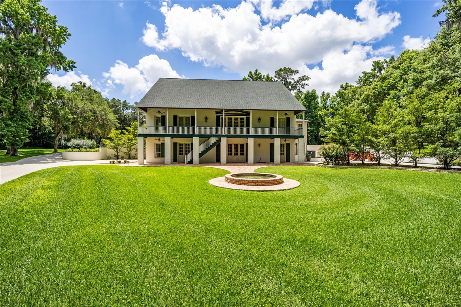 Hunt Country Style home located in the quaint gated SW Ocala equestrian subdivision of Polo Lane. Situated on just under 6 wooded and parklike acres, this one of a kind custom home combines rustic charm and traditional craftsmanship. With views from every room and room for everyone, this spacious and well appointed retreat offers five en-suite bedrooms. Built with the same practicality and design advantages as a hunt country bank barn, this multilevel home has easy access to two levels. Take the winding drive over the brick bridge, past the brick fountain courtyard to park in the cohesively designed covered carport at the back of the home for easy entry to the main level or park at the front parking area of the home for easy access to the lower level. Guests may choose to take stairs to the main level porch entrance. The main level entry great room features a striking old English country aesthetic featuring rustic beams, solid wood floors, and brick architecture with a fireplace flanked by French doors. The dining room embodies rustic elegance featuring a beautiful wall of windows, stunning pool views, wood beams, and a brick wall with French doors leading to the porch. The adjacent custom kitchen offers designer appliances that make cooking and hosting seamless. Laundry is a breeze, literally in this laundry room, just open the French doors to the shady porch and let the fresh air in. Tucked across off the great room, is the primary suite, junior suite and guest bathroom. Imagine waking up and stepping outside the French doors to a porch from either suite. The spacious primary suite features double closets and an old world style bathroom with lovely accent beams, aged limestone tiles, windowed garden tub and walk-in shower. Back to the great room off the front entry, ascend the stairs to discover three generous sized additional en-suite bedrooms and a cozy loft space. Back down stairs to the main living level, down the hall, past the kitchen, a solid wood circular staircase winds its way down to the lower level entry hall. The lower level will delight any enthusiast featuring a pristine two car garage and a pristine workshop flanking two versatile spaces, complemented by another full bath. Perfect for a home office, studio and or a fitness space and provides direct access to the lower front porch and lawn. This home offers French doors and several porch options for enjoyment and relaxation. The beautifully weathered wood back porch, overlooks the pool that blends seamlessly with its natural surroundings and offers timeless style in reclaimed brick and salted concrete. Extensively landscaped, meticulously maintained, tremendous storage and a generator for peace of mind, this is a one of a kind retreat that has it all for families and friends to make lasting memories. Newer roof, mechanics for house and pool, generator and more. Convenient access to grocery, shopping, downtown, medical and less than 8 miles to equestrian venues and golf. Let us give you a personalized and detailed tour.