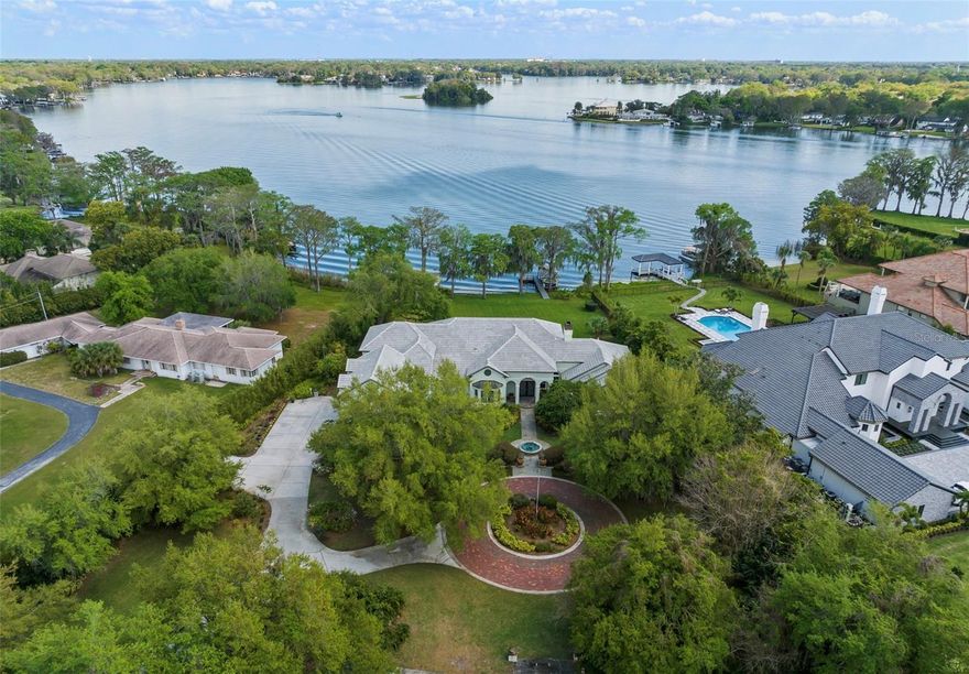 Embrace the epitome of luxury living with this extraordinary lakefront estate located in the heart of Maitland, where endless possibilities await. This expansive custom-built residence, spanning nearly 6,000 square feet, presents the rarest of opportunities. Whether you envision moving right in, updating the existing custom residence, or building anew on this coveted 2-acre high-and-dry lakefront lot, the potential is limitless.
The maturely landscaped driveway meanders to a circular paver roundabout leading you to the custom leaded glass entry doors. The foyer makes way to the expansive light filled formal living room boasting high ceilings, a wall of windows, a gas fireplace, and spectacular views of the lush backyard rolling gently down to unobstructed views of Lake Maitland.  The chef’s kitchen, equipped with custom cabinetry, a stunning copper stove hood, double ovens, and spacious countertops, makes way to the open glass breakfast nook inviting you to create a culinary haven tailored to your every desire. Adjacent to the kitchen, lies the formal dining room, complete with slate tile and majestic front garden vistas!
The first-floor primary bedroom, with its panoramic water views, dual walk-in closets, and spa-inspired bathroom, presents an opportunity to enjoy a luxurious retreat that exceeds your expectations. Just outside the primary bedroom is a stately office with custom wood paneling, a morning bar, and two-story bookshelves complete with a sliding ladder and French doors that lead to the covered porch with stunning lake views.  Downstairs, two additional bedrooms and a Jack and Jill bathroom offers ample space for family and guests, while the upstairs in-law suite, complete with a private balcony overlooking the lake provides a spacious family room area, and full kitchenette, making it the perfect retreat for your most coveted guests, they'll never want to leave their very own sanctuary!  The media and game room is second to none boasting an oversized wet bar with counter seating, an additional full bath and a generous closet behind hidden glass doors.
The oversized 4-car garage with a spacious storage room ensures that your vehicle and hobby needs will all be met. The nearby oversized laundry area and mudroom, complete with an additional full bathroom is beyond practical.  Relish in early morning sunrises and daily duck visits from your massive screened-in rear patio, and private composite dock with a covered boat lift assures you appreciate the extraordinary views of Dog Island, Isle of Sicily, and the Winter Park Racquet Club.  The original regulation-size tennis court, partly shaded by an abundance of Florida citrus trees, has the potential for pickleball courts, basketball or multi-sports court, offering a blank slate for creating your ultimate recreational space.
Situated walking distance from famed Luke's Kitchen and Bar, Antonio’s, and other fine restaurants, and with Winter Park’s--Park Avenue Boutiques and restaurants only 2.5 miles away, this extraordinary lakefront estate presents a once-in-a-lifetime opportunity to build or update your dream home in one of Central Florida’s most sought-after locations. Seize this chance to make your mark on luxury waterfront living and create a legacy that will endure for generations to come!