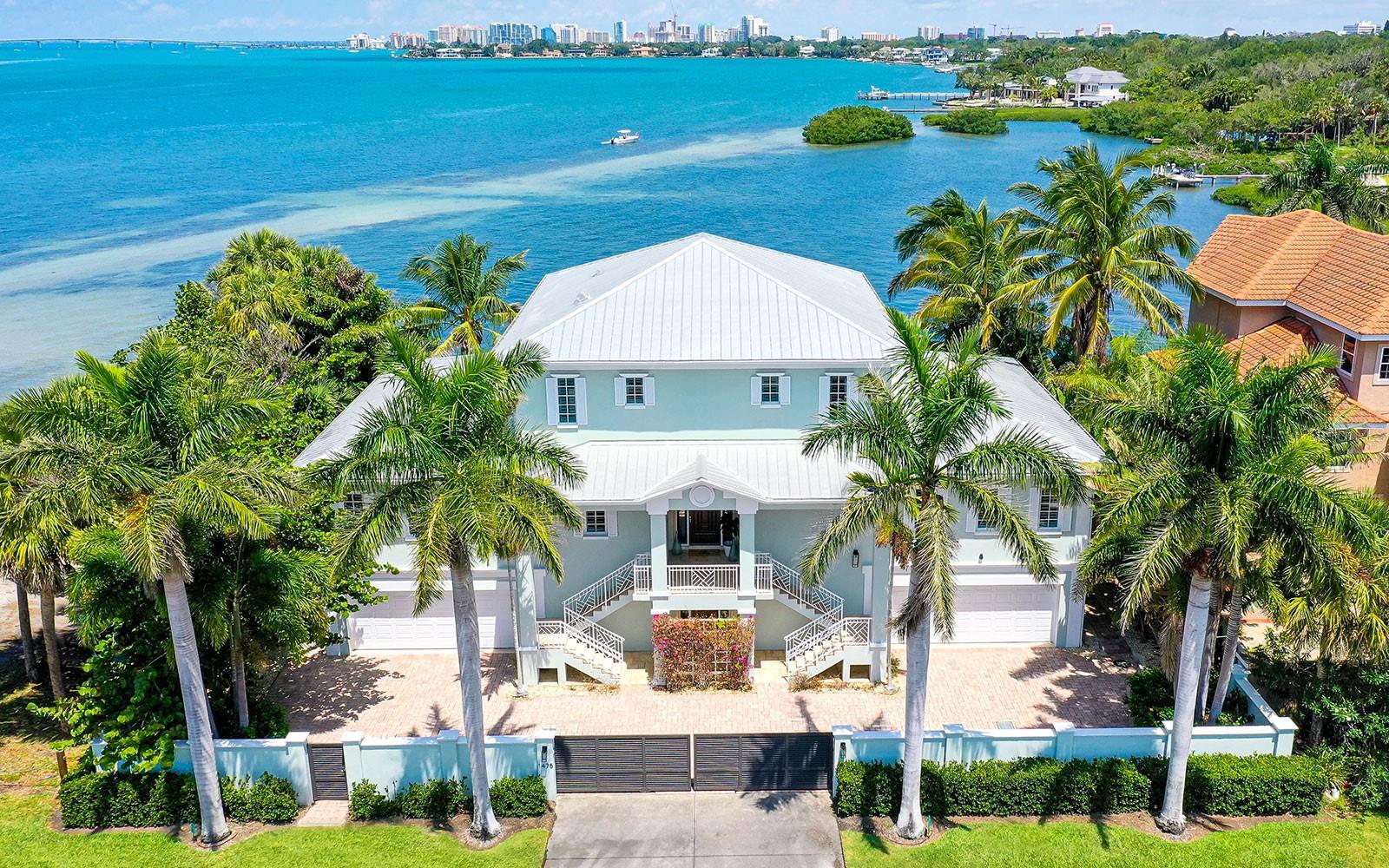This Sarasota bayfront home is located at the gateway to Siesta Key with panoramic waterfront views of Sarasota Bay, John Ringling Bridge and downtown skyline. Every living space has an amazing view in this extremely well-built, three-story custom bayfront home. This home of 3,750 square feet features a semi-open floor plan with elevator access to all levels. Expansive walls of glass, covered balconies and bayside pool orient this home to the year-round blue skies, gulf breezes and spectacular sunsets famously found in Sarasota. The home’s distinctive interior is marked by the timeless appeal of new engineered hardwood flooring and feels expansive, being flooded with waterfront-facing glass. Breathe easy with clean indoor air from the UV Micropure air purifier in the main air conditioning. The second floor is the main living level, with gourmet kitchen flowing into the family, dining and living rooms that all open to a spacious balcony overlooking the pool and amazing views. The kitchen features a center island with double-granite textured-edge countertops and high-end appliances. This floor also features three en-suite bedrooms, an office with access from the living room and front door, plus a laundry room off the kitchen. Stairs or an elevator lead you up to the private owners’ retreat on the third floor where you have luxurious living space enhanced by an extra-large bath, closet with laundry station, and balcony with splendid bay and city views. Ride the elevator down to the first floor for a workout in the exercise room or set up your favorite games in the large game room. This waterfront home opens to an outdoor setting where exceptional living continues. The covered lanai space features multiple seating areas for entertaining guests and an outdoor kitchen to grill your fresh catch of the day. The heated pool features a seating ledge offering yet another vantage point for the bay and city views. The waterfront is ideal to enjoy paddle boarding, kayaking or canoeing, and the davits on the seawall allow jet skis, a jet boat or skiff. This home features dual two-car garages to house your toys. Its convenient central location is just 10 minutes to Siesta Key Beach and downtown Sarasota with all it has to offer.