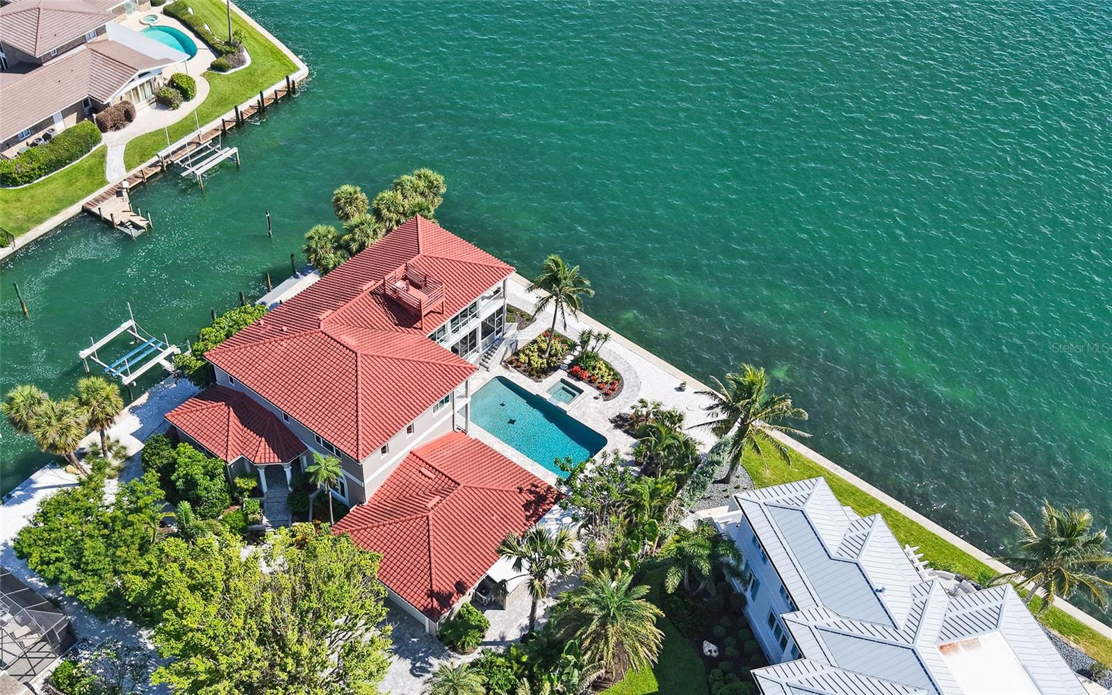 Welcome to 585 Gunwale Lane, a rare, full-bayfront offering in the desirable community of Country Club Shores on southern end of Longboat Key. On a .36-acre bayfront parcel with 117 feet on Sarasota Bay and 123 feet on a deepwater canal, this residence is a boater’s paradise. A newer seawall and 58-foot dock (2022) with a 24,000-pound boat lift assure easy access to Sarasota Bay and the Gulf of Mexico. On the bay side, Ghost Island sandbar emerges at low tide, creating a natural haven that attracts abundant wildlife and offers fantastic shelling. It also serves as a natural barrier, providing protection during storms. On the Gulf side, deeded access to an exclusive community beach is just a half-mile away. Whether you’re heading out for a day on the water or popping over to St. Armands Circle for dinner and shopping, this home puts you in the center of it all. The residence spans 4,733 square feet and includes three bedrooms and three-and-a-half baths. A soaring 20-foot ceiling defines the living room, where wall-to-wall built-ins create a refined focal point. The dining room opens to a remodeled kitchen outfitted with Graber wood cabinetry and professional-grade Frigidaire appliances. The primary bedroom is on the second floor, featuring a private bayfront balcony, dual walk-in closets, and an adjoining 270-square-foot bonus room ideal for a home office or wellness retreat. Outdoor amenities include a bayfront pool and spa for enjoying Florida sunsets. Additional highlights include impact-resistant windows and doors, and a two-car garage. For those who want to design and build their dream home, this property offers a spectacular location. Imagine a custom rooftop deck with breathtaking 360-degree views of the bay, Gulf, and downtown Sarasota. This is an opportunity to create something extraordinary. This exceptional property presents a rare opportunity to park your boat in the backyard and join the privileged few who call this well-established neighborhood home. By land or by sea, welcome to your fabulous Florida lifestyle!