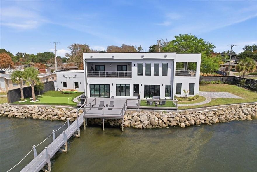 Modern Waterfront Masterpiece on Merritt Island with 142 Feet of Direct Indian River Frontage—this 2024-built, two-story luxury residence offers a rare combination of cutting-edge design, solid construction, and true Florida waterfront living. Built with full concrete block construction on both levels and topped with a commercial-grade roof, this home delivers both style and substance in a way that is virtually unmatched on the island. Featuring 5 bedrooms, 4 full bathrooms, and a 2-car garage, the property comes fully furnished and move-in ready, making it ideal as a primary residence or a high-end vacation retreat. Inside, you’ll find designer finishes throughout, including a sleek modern kitchen, custom built-in closets, high-end lighting, motorized shades, smart home features, and smart toilets in multiple bathrooms. The expansive upstairs primary suite is a true showpiece, offering a private covered terrace overlooking the water, a massive wraparound closet, and a spa-inspired bathroom with a dramatic wall of designer tile and luxury shower. Outdoor living is just as impressive, with a large side yard, putting green, and a covered boat dock with lift plus a jet ski dock—perfect for enjoying deep water access to the Indian River and quick routes to the Atlantic Ocean or cruising toward Cocoa Village. From your west-facing balconies, take in breathtaking sunsets along with daily sightings of dolphins, manatees, and pelicans. Located on prestigious South Tropical Trail, just minutes to Cocoa Village, approximately 45 minutes to Orlando International Airport, and about an hour to Disney World, this home offers a rare blend of privacy, accessibility, and lifestyle. Truly a one-of-a-kind, turnkey modern waterfront property in Central Florida.