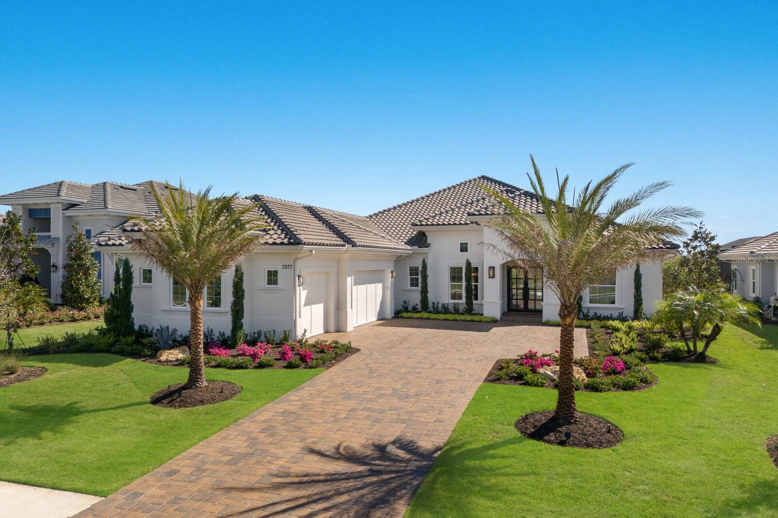 Curated by an interior designer, this professionally refined residence was built in 2024 on a stunning lot inside the exclusive gated community of The Lake Club boasting surrounding views from the front and back of the home to enjoy both sunrises and sunsets. Encompassing 3,754 square feet of open one-story living, this customized Stock Home built in 2024 exudes stylishly planned indoor and outdoor spaces, accentuated volume ceilings, skillfully selected finishes, Restoration Hardware light fixtures, and, of course, IMPACT windows/doors/sliders.
An expansive outdoor retreat elevates the Florida living experience with a panoramic screened lanai, extensive open and under cover spaces grounded with travertine pavers, soaring ceilings, full summer kitchen, PebbleTec heated saltwater pool/spa with sun shelf, gas fireplace and even a fenced dog run. Ten foot impact glass sliders seamlessly connect the outdoor oasis to a luxuriantly welcoming great room, dining area and gourmet kitchen with sumptuous wood floors crowned with stunning ceiling treatments, accent wall, and designer light fixtures creating a sophisticated and open continuity of space. Meanwhile the kitchen further accentuates with dual layers of wood cabinetry, elevated quartz counters, high-performance Jenn-Air appliances, induction cook top yet also pre-plumbed for gas, and a wet bar with wine fridge off the formal dining room. An impressive club room directly off lanai beckons for entertaining with soaring ceilings and windows with glorious views beyond.
Relax and unwind in the owner’s quarters positioned on a private wing, offering double tray ceilings, large scale windows, direct lanai access, wood flooring, two oversized walk-in customized closets, privacy remote screens, and a luxuriously appointed bath with dual station vanity, an oversized shower with designer tile, a large soaking tub, and separate water closet. On a separate wing of the home there are three additional guest suites generous in size, all with walk-in closets, two offer ensuite full baths, while the third guest room is just off the home’s fourth full bath. The residence also offers an impressive office behind double-entry doors just off the entry foyer. Other notable highlights of this newly built all-encompassing 5,963 total square foot residence includes a brilliantly finished laundry room, beautiful built-in mud room area, a fenced in dog run, double-insulated walls in the primary suite/laundry room and office, tankless water heater, all impact windows and doors, water filtration system, reverse osmosis in the kitchen, Smarthome automation, and an oversized three car garage with electric car charging station.
This bespoke offering defines modern refinement beckoning a lifestyle fulfilled and the pinnacle of luxury living in The Lake Club, where residents enjoy access to a wealth of amenities, including two resort-style heated pools, Grande Clubhouse with fine dining and bar area, a fitness center, spa, tennis courts, pickleball, a playground, dog park, and services of a full-time concierge and activities director.