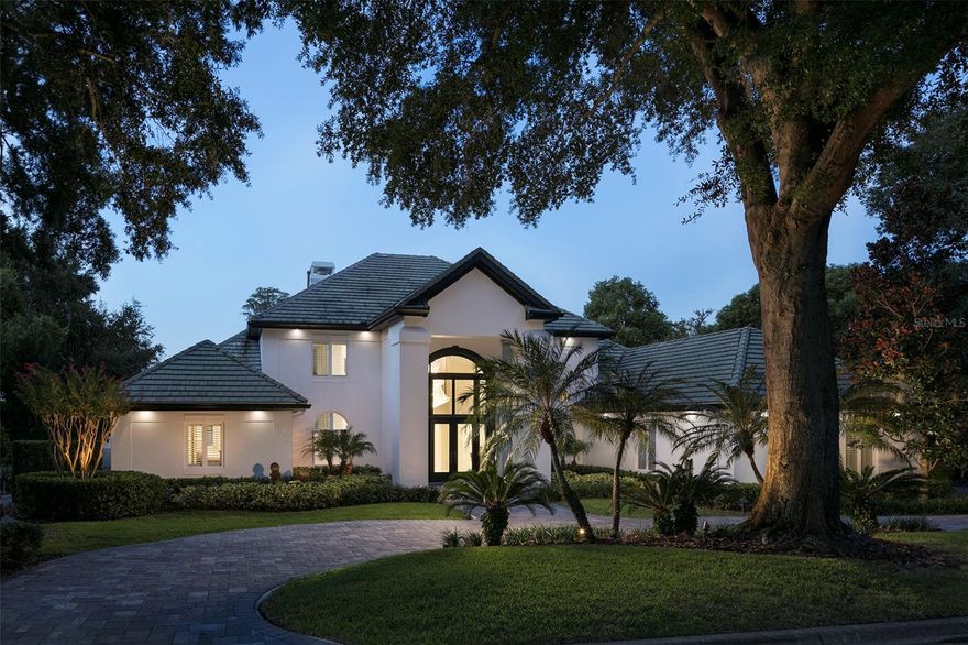 Within the gates of Isleworth Golf & Country Club, along the shores of Lake Chase, this exceptional lakefront offers a refined and contemporary waterfront lifestyle. Ideally positioned near the driving range and just moments from Isleworth’s racquet center, clubhouse, fitness facilities, dining, and pool, the residence combines privacy with convenience.Designed by renowned architect Mark Nasrallah, the home spans more than 7,100 square feet and showcases sophisticated detailing and elevated finishes throughout. A grand foyer introduces the residence with a sweeping floating staircase and dramatic tiered crystal chandelier, leading into the formal living room where soaring ceilings, dual chandeliers, a fireplace, and expansive lake views create an impressive yet inviting setting.Marble flooring transitions seamlessly into the home’s primary living spaces, where rich hardwood floors enhance the warmth of the open-concept kitchen, casual dining area, and family room. The kitchen is both functional and elegant, featuring an oversized island, custom cabinetry, quarried quartz countertops, and professional-grade appliances by Wolf, Sub-Zero, and Bosch. A contemporary, temperature-controlled wine room accommodating over 100 bottles adds a distinctive touch. Architectural millwork in a diamond pattern defines the dining space, while custom media built-ins in the family room enhance the home’s cohesive design. Both areas open effortlessly to the lanai and pool deck.The primary suite serves as a private retreat, complete with a sitting area, designer lighting, and a spa-inspired bath featuring a soaking tub, expansive dual vanities, and a large walk-in shower. Additional interior highlights include a modern office with custom built-ins and private pool access, as well as a spacious game room with a full bar and captivating water views. Outdoors, the covered lanai extends to a resort-style pool and spa, surrounded by generous lounging areas and complemented by the private boat dock - creating an unparalleled setting for boating, entertaining, and year-round enjoyment in Florida's tropical climate.