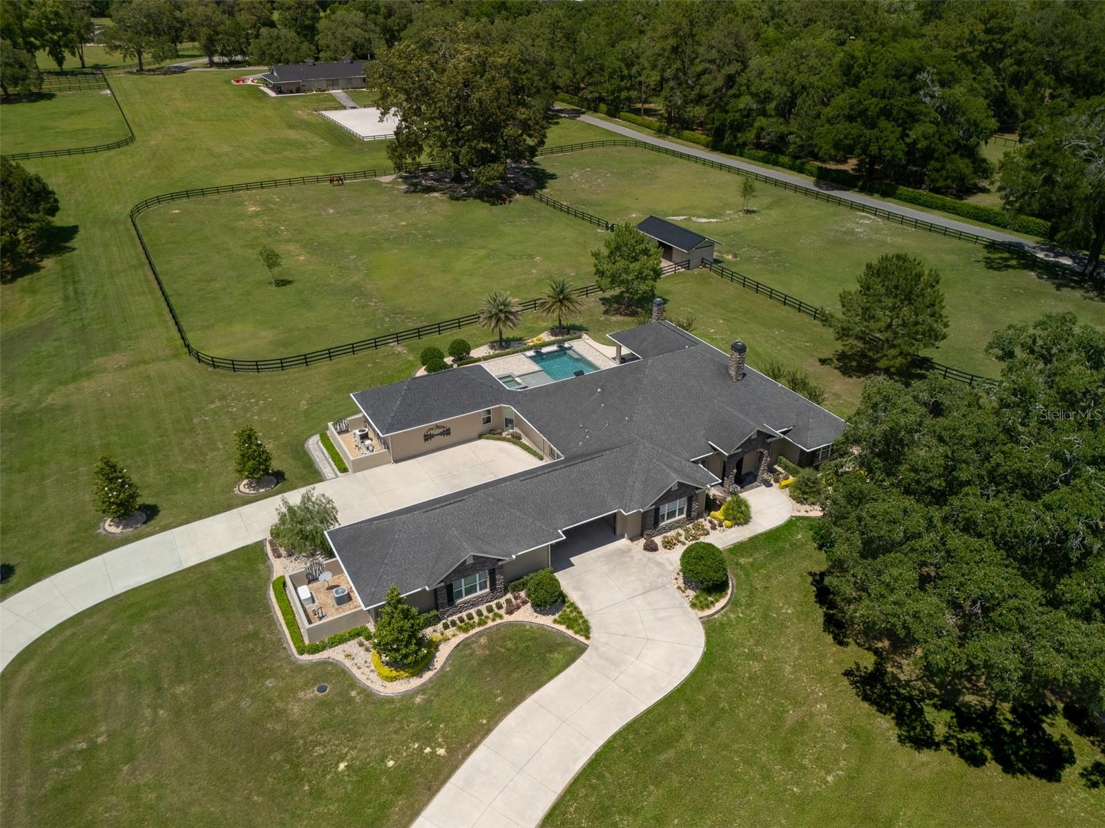 Located in the Farmland Preservation District of NW Ocala, this 27.53-acre equestrian estate is just 10 minutes from the World Equestrian Center and 8 minutes from HITS! Fully renovated and expanded in 2022, the property blends luxury living with world-class equestrian facilities. Custom gates open to landscaped grounds with two private paved drives—one to the main residence, the other to the barns, guest home, and operational buildings. The concrete block, center-aisle main barn includes a sprinkler system, brick pavers, tongue-and-groove ceilings, 8 matted stalls with fans and water, foaling stall, 2 hot/cold wash racks, and a climate controlled tack/feed room with half bath and laundry. A professional arena with nylon footing and advanced drainage ensures year-round use. Attached is a 1350 square foot 2-bedroom, 2-bath residence with a wraparound porch, expansive kitchen, and laundry—ideal for guests or staff. Additional amenities include a brick-paver fire pit area, three paved RV sites with full hook-ups, plus a large insulated metal building with double pull-through bays, carport, and porch. Two more barns add six stalls with electricity. The 4-bedroom, 3-bath main home features a great room with linear fireplace, formal dining, office with built-ins, chef’s kitchen with oversized island, high-end appliances, and premium finishes. The owner’s suite offers a spa-inspired bath and custom walk-in closet with concealed safe. Outdoor living includes a heated saltwater pool with sun shelf, spa, fire/water bowls, and expansive paver lanai with outdoor kitchen, gas fireplace, TV and sound system. Other highlights are a 3-car garage, Porte Cochere, whole-house generator, solar with Tesla battery backup for outbuildings, security cameras, and 12 fenced pastures with room to expand. This estate delivers unmatched equestrian infrastructure and modern amenities, minutes from Ocala’s premier venues!
