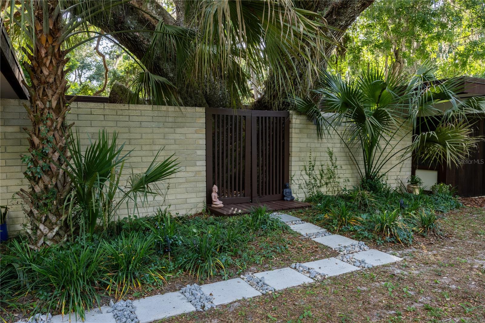 Here is your chance to live in a rare Mid-Century Modern gem. With its clean lines and harmonious integration with nature, the 1966 Haynes Residence is a Mid-Century Modern masterpiece. Designed by Architect Harry Merritt and inspired by the Case Study Houses of Southern California and Frank Lloyd Wright’s Usonian houses, this courtyard home embodies tranquility and architectural clarity with a palette of redwood siding, Ocala block walls and terrazzo floors. Its expansive glass walls look out over a 1.65-acre property, which backs onto undisturbed forest one block from Newnan's Lake. For lease, This 3 bedroom plus office, 2 bathroom home respects its original design while breathing new life into its iconic elements with subtle sophistication. Available now. Extensive updates include a new commercial grade roof, repaired eaves, improvements to the plumbing and electrical systems, paint, wallpaper and meticulously restored terrazzo floors. The home is centered on a majestic Live Oak tree in the courtyard, which is visible from every living space through continuous glass walls. The courtyard’s deck and generous eaves create a dynamic outdoor living space that connects to the kitchen and dining rooms through a wall of sliding glass doors. The kitchen has been updated with stainless steel appliances, refinished wood cabinets, center island with breakfast bar and two pantries. Off the kitchen is the dining room with a George Nelson Bubble chandelier, recessed built-in buffet and large windows overlooking the expansive backyard. Around the corner is the dramatic sunken living room with wood burning fireplace and custom metal hood. This space features signature elements of Merritt's designs: its lofty height, Ocala block built-in seating and fireplace mantle, and walls of glass offering panoramic views. Around the corner is the more intimate family room with built-in seating (featuring hidden storage), windows to the backyard and another set of sliding glass doors to the courtyard. A hallway leads to an updated, full guest bathroom and two guest bedrooms with walls of windows overlooking the rear garden. At the end of the hall is the large primary suite. This room has a built-in vanity with a wall of shelves. All the bedrooms have custom closet systems by California Closets. The master bedroom has another Merritt signature feature, a wall of Redwood siding and clerestory windows. The Primary Suite includes an en suite bathroom with an updated shower with seamless glass enclosure and vanity with new sink. Both the primary bathroom and the family room connect to an intimate office with another wall of Redwood siding, built-in desk and flexible storage space. There are two septic systems and a well with a water purification system. The property is a serene, low maintenance space that embraces nature. The Live Oak–one of the largest recorded in the Southeastern United States, anchors the site, and its massive canopy shades the home. Deer pass quietly at dawn, owls nest in the limbs, and bald eagles soar overhead. Magnolia Estates is a peaceful sanctuary just three miles from downtown Gainesville and an easy drive to the University of Florida and UF Health. $54 application fee. First, last and security deposit. Includes lawn maintenance and pest control.