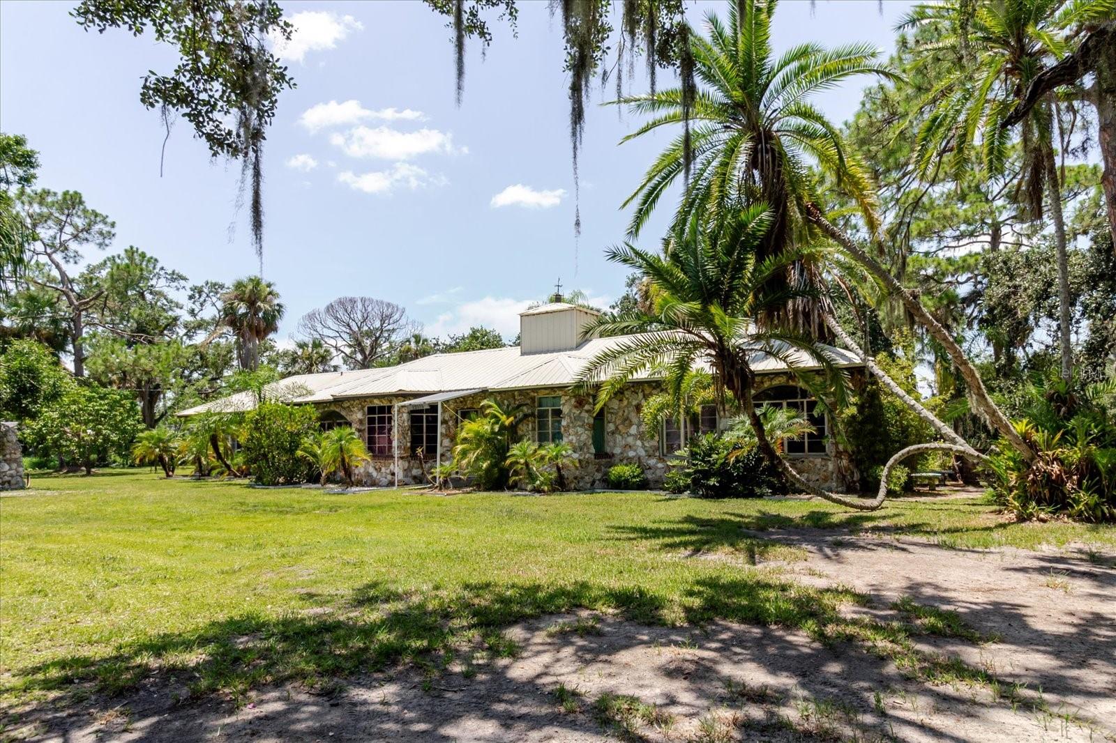 Welcome to 12115 S US Highway 41 in Gibsonton, Florida—a rare opportunity to own a versatile 3-acre waterfront property with approximately 270 feet of highway frontage. This one-of-a-kind ranch-style stone home offers both rustic charm and incredible flexibility for residential, agricultural, or potential commercial use (buyer to verify zoning). The 3-bedroom, 3-bath home features soaring ceilings, a massive stone fireplace in the great room, and durable stone flooring in high-traffic areas. A private home office with custom wood shelving and French doors opens to the living room, making it ideal for remote work or a quiet study. The spacious utility room adds to the home’s functionality.
Outdoors, the property is a dream for homesteaders, animal lovers, or anyone looking for space and privacy. A detached concrete block workshop measuring approximately 22 by 34 feet with 20-foot ceilings offers ample room for vehicles, equipment, or business storage. The land is fully equipped with a working barn suitable for large or small animals, a chicken coop, pig pen, multiple fenced dog kennels, and a large fenced pasture for grazing. A detached drive-through barn allows easy access for trailers or farm machinery. Beautiful mature trees provide ample shade, while a charming flower garden adds to the natural serenity. The property also backs up to a shallow waterway offering access to the bay—perfect for kayaking or simply enjoying the waterfront atmosphere from your backyard.
Located adjacent to a 6.58-acre county park, this property offers enhanced privacy and open space while remaining conveniently close to major roads and amenities. Hurricane protection systems are in place for the windows, offering peace of mind. Whether you're looking to create a peaceful homestead, run a small farm, or explore commercial possibilities, this property offers unmatched potential in a growing area.