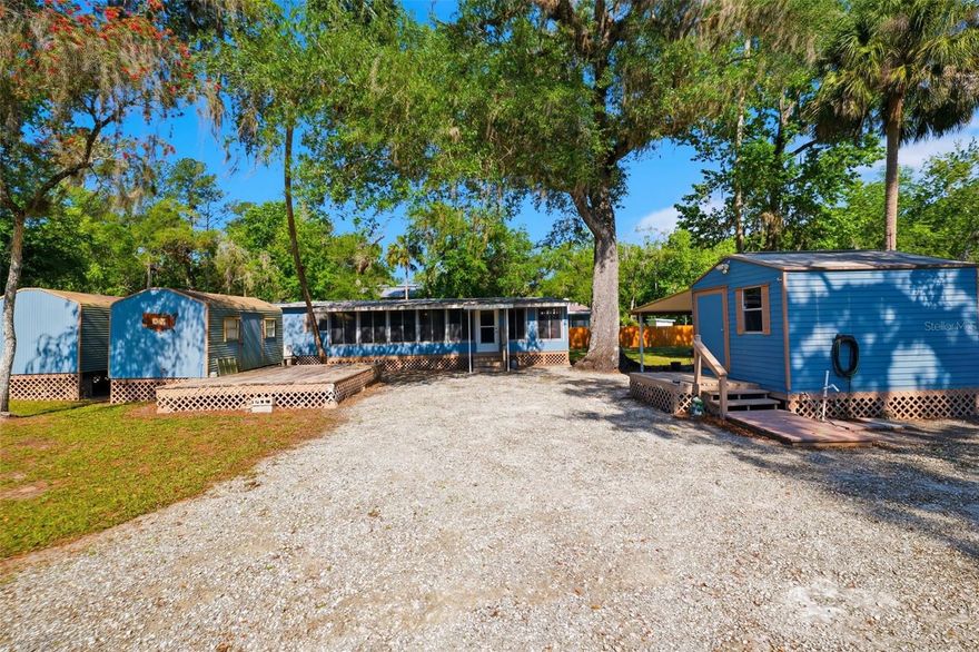 Welcome to your own private riverfront retreat on the Withlacoochee River, where nature, relaxation, and opportunity come together on a beautifully shaded 0.89-acre property surrounded by mature trees. This fully fenced property offers direct water access, a private boat ramp, and a spacious deck right on the river--perfect for tying up your boat, enjoying peaceful views, or unwinding by the water. A fire pit, riverside bench, and a cement patio tucked beneath the trees create multiple outdoor spaces to relax and take in the serene setting. This unique offering comes fully furnished, with most everything conveying--including boats, a travel trailer, hot tub, and more--making it truly move-in or rental ready. Additional features include three sheds (one equipped with a refrigerator, washer and dryer, and tools), an RV carport, a separate boat carport, and a water softener that conveys with the home. Inside, the home welcomes you through a large, enclosed sunroom filled with natural light. This inviting space features walls of sliding windows overlooking the yard, a decorative beamed ceiling, well-maintained carpet, and its own air conditioning--creating a comfortable, year-round living area. From there, step into the main family room, where crown molding, chair rail detailing, and beadboard wainscoting add warmth and character. Luxury vinyl flooring runs throughout the home, offering both durability and style. The kitchen sits just off this space and features all-white cabinetry and appliances, with a pass-through window connecting back to the sunroom for an open, connected feel. A hallway with built-in storage and shelving leads to the rest of the home, including a spacious formal living room with a wall of windows, built-in shelving, decorative beamed ceiling, and direct access to the backyard. This versatile space also includes a large walk-in closet, adding flexibility for storage or additional use. The home includes two comfortable bedrooms and a full bathroom with a step-in shower, built-in shelving, a single white vanity, and a window for natural light. Whether you're looking for a weekend getaway, full-time residence, or income-producing opportunity, this riverfront property offers incredible value with its included amenities, multiple storage options, and direct access to the water--all in a peaceful, natural setting.