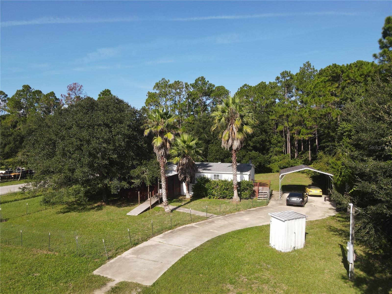 Country Charm on Nearly an Acre in Daytona North - This spacious 3-bedroom, 2-bath mobile home sits on almost an acre, offering the perfect blend of comfort and country living. A large covered, screened front porch welcomes you inside to a cozy living room and a separate dining area. The home also boasts a generous great room/kitchen combo featuring a warm wood burning fireplace, center island, and ample counter space—ideal for gatherings and everyday living. The primary suite offers a relaxing retreat with a garden tub, walk-in shower, and dual vanities. Outdoor living continues with a side porch and a rear porch overlooking the serene property. A large carport with space for up to four vehicles, a shed, and a pump shed provide additional ample storage. Also, part of the yard is fenced, which makes it perfect for pets. With room for your toys and plenty of open space, this home is ready for you to enjoy the peaceful country lifestyle of Daytona North. The entrance to the front porch also features a wheelchair ramp.
