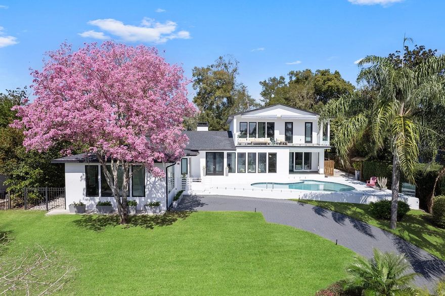 This stunning contemporary lakefront residence, completed in 2019, offers almost 6,000 square feet of refined living space with magnificent elevated views of Lake Catherine. Thoughtfully designed with elegant finishes, this two-story, five-bedroom, 5.5-bath residence, plus office/media room and open flex/lounge area that showcases a bright/open floor plan enjoying expansive walls of glass windows/doors that frame the serene waterfront setting. The main level features sleek porcelain tile flooring, soaring ceilings, and sun-drenched interiors. Two separate back-to-back fireplaces connect the formal dining area and living room, while the spacious family room is bathed in natural light. The modern kitchen boasts a large island, high-end appliances, a hidden pantry and laundry room, and a built-in coffee maker. The first-floor primary suite offers lake views, a custom walk-in closet and a spa-like bath with dual sinks, a walk-in shower and a jetted soaking tub. A versatile flex space adjacent to the suite is ideal for a fitness area, office or private retreat. A floating staircase leads to the second level, where a generous bonus room/game room, two additional bedroom suites with walk-in closets and en-suite baths, and another flex room await. The expansive second-floor balcony overlooks the sleek glass-railed pool and provides uninterrupted lake views. A separate parcel across the street includes a private covered dock on the 21-acre Lake Catherine, ideal for kayaking and paddleboarding. The two-car garage, accessed through a gated rear entry, adds convenience and security. In a tranquil, private setting, yet minutes from Maitland’s cultural corridor as well as the vibrant shopping and dining of Park Avenue, this exceptional property seamlessly blends contemporary luxury with lakeside tranquility.