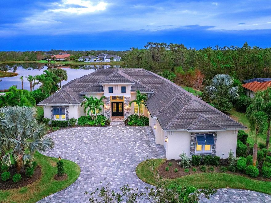 This 2020 custom-built lakefront home is in the prestigious gated enclave of Nicklaus Manor within The Concession. The luxurious residence spans 3,674 square feet of refined living space with exceptional craftsmanship and design. The grand entry is framed by an oversized paver circular driveway, lush landscaping with lighting, and a travertine porch with stone columns and shutters. Through the double iron doors with textured privacy glass, the foyer boasts an archway with custom wood casing, complementing the engineered hardwood floors throughout. The great room features a custom ceiling with wood-wrapped beams, a shiplap accent wall with a linear fireplace and solid reclaimed wood mantel. A wet bar with white cabinetry, granite countertops, a dual-zone wine refrigerator, prep sink and wood shelving makes entertaining effortless. The gourmet kitchen blends functionality with design. A dropped soffit ceiling defines the area. Granite countertops with a tile backsplash line the perimeter and numerous outlets are integrated for convenience. Stainless steel Monogram appliances cater to culinary enthusiasts. A coffee bar with exposed shelving and integrated lighting is complete with a stunning tiled wall. Three oversized windows above the range fill the space with natural light and a shiplap accent wall above the cabinets and coffee bar adds charm. The island features a thick-edge granite countertop with an extended butcher block dining area, ideal for casual meals or entertaining. A spacious walk-in pantry with wood shelving provides storage. The open-concept flows to the dining room, which features a designer chandelier and zero-corner sliders. The primary suite features a double-door entry, custom accent wall, plantation shutters and French doors leading to the lanai. The suite features two walk-in closets, one is a massive 14-by-13-foot closet with a large window. The spa-like bath offers dual vanities with marble countertops, a freestanding soaking tub, and an enormous Roman shower with triple head shower system and niches. All bedrooms are in separate wings for extra privacy. Guest bedrooms each feature large windows with plantation shutters, walk-in closets, and en-suite baths featuring vanities with quartz and marble countertops. A versatile bonus room showcases wainscoting accent walls, a tray ceiling with wood-wrapped beams, designer lighting and sliders. Step outside to an expansive lanai that boasts a Wi-Fi-enabled heated saltwater pool and spa with a sun shelf, lighted water bowls and a panoramic screen offering a lake view. The outdoor kitchen includes a grill, vent hood, refrigerator, granite countertops and backsplash and Synergy® inlay wood ceilings in the covered areas. The lanai is surrounded by preserves on both sides. The spacious laundry room boasts quartz countertops, custom cabinetry, a tile backsplash and another refrigerator. The oversized three-car garage offers ample storage with a ceiling storage rack. Every detail of this home reflects quality including custom ceilings with crown molding, detailed casing around windows and doors, hurricane-rated windows and doors, attic encapsulation, Control4 smart home compatibility, a Wi-Fi-enabled hot water recirculation system and sprinkler system. The Concession, home to the 2021 PGA Tour World Golf Championship and the 2023 PGA World Champions Cup, is one of the prestigious golf communities in the country and provides the ideal tranquil setting.
