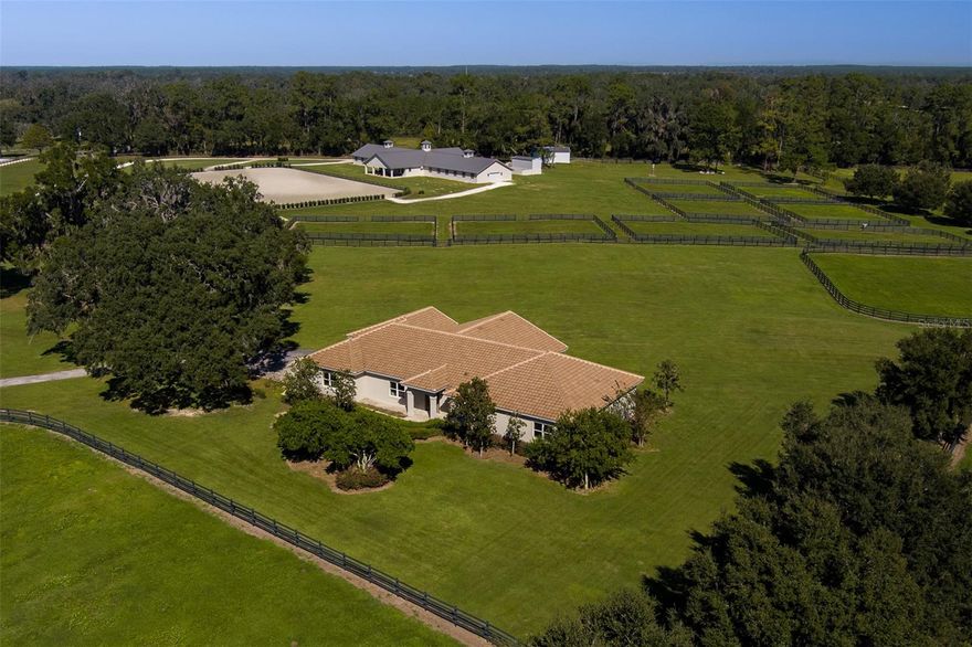 Situated 15 minutes from the World Equestrian Center and 5 minutes from HITS, this 42+ acre farm benefits from a prime location within Ocala’s leading equestrian community. The property is fully fenced and gated, with mature oak trees that create a beautiful and private setting from the moment you arrive. The farm’s equestrian amenities are extensive and thoughtfully designed. A well-appointed, center-aisle 20-stall barn features comfort mats, wash racks, a dedicated tack room, half bathroom, and a spacious laundry room. A private apartment/office within the barn includes its own kitchen, bedroom, full bath, and half bath, providing excellent flexibility for on-site staff or guests. Multiple lush paddocks offer ample turnout, and the 150x250 arena complete with all weather fiber footing delivers a quality riding surface suited for training and daily exercise. A separate 2-bay shop adds valuable storage and equipment space. The main residence is warm, inviting, and finished with thoughtful details. It includes 3 bedrooms, 2 full bathrooms, and 1 half bathroom. Tray ceilings and natural light enhance the comfortable interior. The updated kitchen features modern appliances, generous countertop space, and a practical layout fitting for both everyday meals and entertaining. French doors lead to a charming back porch outfitted with an outdoor kitchen, a fire pit, and a relaxing seating area overlooking the property. A separate guest house offers additional accommodations with 3 bedrooms, 1 bathroom, a full kitchen, living area, and laundry room, ideal for guests, family, or farm staff. With its prime location, appealing setting, and well-rounded amenities, this property provides a functional and welcoming environment!