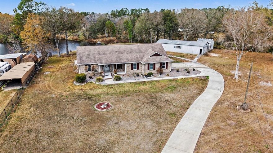 Welcome to 31835 Cromwell in Wesley Chapel — a unique 1.72-acre waterfront property offering privacy, functionality, and exceptional versatility with no HOA or CDD. This 3-bedroom, 3-bath home features hardwood floors in the dining room and sunken formal living room, tile throughout the main living areas, and multiple skylights that fill the home with natural light. A windowed sunroom under heat and air provides additional flexible living space overlooking the pond and pool. The living area is anchored by a fireplace, and the kitchen includes granite counters and a hidden gem pantry with extensive cascading shelving. Kitchen also has a floating/moveable island, black appliances, and a breakfast bar. The primary suite includes an updated bath with a garden tub, separate shower, and thoughtful finishes. Major updates include a roof replaced in 2018 and A/C installed in 2019. The home is also equipped with a water conditioner system and reverse osmosis at the kitchen faucet. Outdoors, enjoy an in-ground pool and tranquil pond frontage within a fully fenced property secured by an electric gate. The pool area features a 10’ retractable awning. The property is serviced by a well and septic and includes a 26kW whole-house generator that can power the home and both workshops. For those needing workspace or storage, the two detached workshops are a standout feature. The larger 60' x 25' workshop offers A/C, heat, electric, private office space, and a half bath, while the second 24' x 18' building also includes electric — ideal for hobbies, business use, equipment storage, or additional storage needs. A rare opportunity to own acreage with water frontage, extensive improvements, and room to live and work — all in a convenient Wesley Chapel location.