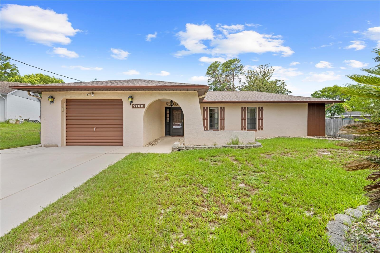 Welcome to 9102 Lamborn Street—a well-loved, original-owner home located on an oversized 0.30-acre lot in the heart of Spring Hill. This cozy 2-bedroom, 2-bathroom home offers 1,143 square feet of living space with a functional split floor plan and plenty of potential to add your own personal touch. As you enter, you're greeted by the main living area with carpet and a spacious dining area just off the back. The kitchen is tucked to the left and features original Formica countertops, classic cabinetry, linoleum flooring, and all major appliances. A sliding glass door off the dining area leads to a large covered and screened lanai, offering the perfect indoor-outdoor connection for relaxing or entertaining. The primary suite is located on one side of the home for privacy and features vinyl plank flooring that extends into the en-suite bathroom. The guest bedroom is situated on the opposite side of the home with its own full bath and can be closed off with a pocket door—ideal for guests or a home office. The guest bedroom has carpet flooring and is spacious and bright. Outside, enjoy a large backyard with plenty of space to create your own oasis—garden, play area, or even a future pool. With no HOA or CDD, you have the freedom to make it your own. The 1-car garage and extended driveway provide ample parking. Located just minutes from shopping, dining, hospitals, Pine Island Park, Rogers Park, and Weeki Wachee Springs State Park, this property is perfect for first-time buyers or investors looking for a great opportunity in a convenient location. Come explore the potential—schedule your showing today!