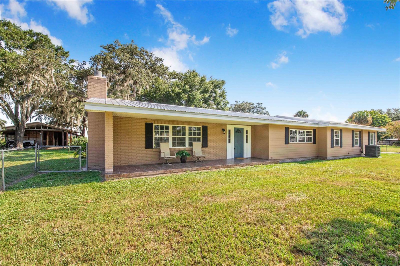 One or more photo(s) has been virtually staged. Welcome to your private retreat on 4.93 high and dry acres, zoned agricultural/residential and perfect for those seeking space, versatility, and comfort. This beautifully maintained 3-bedroom, 2-bath home offers 2,403 sq. ft. of total living area and was built in 1976 with a durable gable metal roof.
The expansive 27’ x 39’ master suite is a true sanctuary, featuring double custom closets, double bathroom vanities, a jetted bathtub, and a water closet. The spacious 19’ x 24’ living room is filled with natural light from floor-to-ceiling French windows and showcases a wood-burning fireplace and custom cabinetry. Enjoy energy efficiency and comfort with double-pane windows throughout the home.
Additional features include an attached 2-car garage with storage cabinets, a large 451 sq. ft. covered, screened, and tiled side porch, and a 120 sq. ft. covered, tiled front porch. Recent upgrades include new Mohawk laminate flooring (2025), a new septic tank and drain field (2024), a 4.0-ton AC unit (2023), and a water purification system (2022).
Multiple outbuildings provide ample space for hobbies, storage, and agricultural pursuits:
- 24’ x 40’ detached garage shop with three roll-up bay doors
- 22’ x 50’ pole barn/stable with tack room and working tractor
- 14’ x 70’ shed with mixed-use potential
- 20 ft. standard shipping container
The property features a circular driveway, fully fenced pasture, and is just minutes from the new Shops at the Grove and Publix Center. This unique property offers the perfect blend of rural tranquility and modern convenience—schedule your showing today!