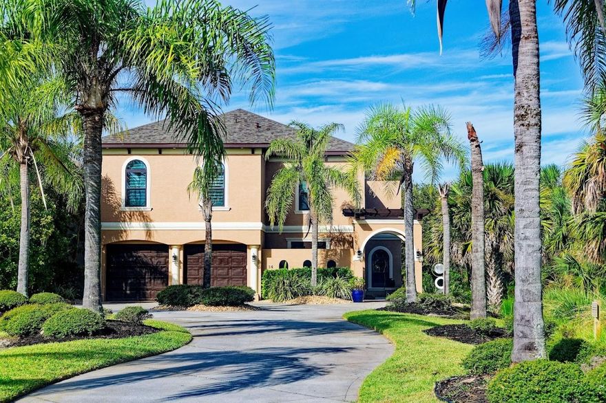 Welcome to 14 Heron Drive, a Mediterranean-style retreat that blends elegance with everyday comfort. Framed by swaying palms, arched windows, and warm wood-tone garage doors, the home makes a lasting first impression. A graceful arched breezeway leads you inside, where a grand entry and sweeping curved staircase set the tone for what’s to come.

Sun-splashed living areas showcase tranquil water views and a striking stacked-stone feature wall with an in-wall fireplace. Cool tile floors transition naturally into rich dark wood in select spaces, adding warmth and character. At the heart of the home, the kitchen invites gatherings with its substantial center island, pendant lighting, granite counters, vent hood, and stainless steel appliances—including double wall ovens. It opens seamlessly to the lanai, making indoor-outdoor living effortless.

Step outside and discover a true Florida haven. Under the screened enclosure, a raised spa bubbles beside serene views of the 125 acre lake. Multiple covered dining and lounge areas with ceiling fans create the perfect setting for relaxed evenings or lively get-togethers. Upstairs, a private screened balcony offers yet another peaceful perch above the water.

The owner’s suite feels like a personal retreat with a tray ceiling, sitting area, and spa-style bath featuring a soaking tub, an expansive walk-in shower, and dual vanities. A customized walk-in closet completes the space. Versatility runs throughout the home, with a dedicated office, bright fitness room, and flexible living areas designed to fit your lifestyle.

With thoughtful exterior lighting that enhances its Mediterranean charm day and night, 14 Heron Drive delivers a sense of resort-style living—welcoming you home in the most inviting way.
