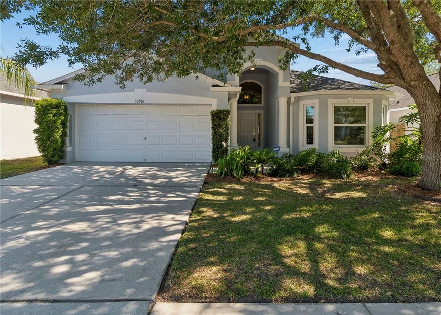 Welcome to this charming single-family home located in the desirable Chapel Pines community of Wesley Chapel. This well-maintained 4-bedroom, 3-bath residence offers 1,810 square feet of comfortable living space with a functional split-bedroom floor plan designed for both privacy and everyday living. Framed by mature oak trees and attractive architectural details, the home offers inviting curb appeal and a warm, welcoming feel from the moment you arrive. Step inside to discover soaring cathedral ceilings, abundant natural light, and an open-concept layout that creates a spacious and airy atmosphere throughout the main living areas. Rich laminate flooring flows through the living spaces, complemented by ceramic tile and carpet for both comfort and durability. The bright living room and dining area seamlessly connect to the kitchen, making the home ideal for entertaining or relaxed daily living. The well-appointed kitchen features ample cabinetry, generous counter space, a closet pantry, breakfast bar seating, and a cozy eat-in dining area perfect for casual meals. Appliances include a range, refrigerator, microwave, dishwasher, disposal, and ice maker, offering both convenience and functionality. Home also features an additional flex room that can be used for a formal dining room, home office, or additional hobby room. The primary suite serves as a peaceful retreat with a spacious layout, walk-in closet, and en-suite bath featuring dual vanities, a garden tub, and a separate shower. Additional two bedrooms are set up for privacy and convenience with jack-and-jill style access to the bathroom. The fourth bedroom is set up to have a separated space for guest complete with their own full bathroom separate from the primary bedroom and two adjacent bedrooms. Sliding glass doors invite natural light indoors while connecting the living area to the covered lanai. The outdoor space features mature landscaping, and room to relax, garden, or enjoy outdoor gatherings. Additional exterior highlights include rain gutters, sidewalk access, a private mailbox, and a north-facing front exposure. Enjoy year-round comfort with central air conditioning and heating, public water and sewer utilities, and the added peace of mind of being located in Flood Zone X. The attached 20x19 two-car garage offers excellent parking and storage space. Chapel Pines is a well-established community with NO CDD fees and low HOA fees of just $85 quarterly, covering grounds maintenance. Conveniently located near shopping, dining, schools, Wiregrass Mall, Tampa Premium Outlets, AdventHealth Wesley Chapel, and major roadways including I-75 and SR-54, this home offers the perfect blend of comfort, convenience, and accessibility in one of Wesley Chapel’s sought-after neighborhoods.