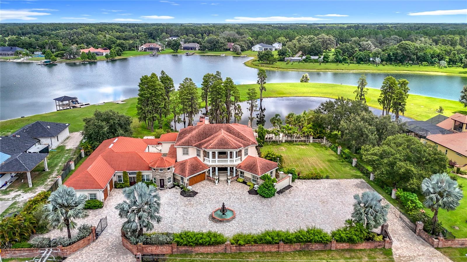 Exquisite Waterfront Estate on Lake Breckenridge – Odessa, FL. Privately gated and masterfully upgraded with over $1.2 million in enhancements, this nearly 4-acre Odessa estate offers 250 feet of direct frontage on the exclusive, skiable Lake Breckenridge. A pavered drive behind two gated entrances leads to a grand arrival court with a fountain. Parking for 10+ vehicles plus a 4-car garage—expandable with lifts—offers space for a collector’s showcase or boat storage.
The 5-bedroom, 3.5-bath custom home showcases cathedral ceilings, a granite fireplace, hardwood floors, plantation shutters, and bright, open living spaces. The gourmet kitchen features double convection ovens, granite counters, decorative backsplash, pine cabinetry, a breakfast nook, and a walk-in pantry. The owner’s suite includes dual walk-in closets, a marble Jacuzzi tub, and separate vanities. Upstairs, custom built-ins, a game room, and balconies with lake views enhance the living experience. The 800sf Bonus Room with soaring 20ft ceilings is perfect for a home theater, a reimagined master suite or in-law/guest suite. Ask us about the secret room for secure storage!
Designed for entertaining, the resort-style grounds feature a sparkling pool and spa, covered pavilion with a chef’s kitchen, grills, brick ovens, and wraparound bar with seating for 10+, plus space designed for dining for 20+ guests. Two firepit areas, a private sandy beach, and an interior courtyard with a fountain add to the ambiance. A walking dock over a tranquil pond is ideal for fishing, coffee, or stargazing. Lake Breckenridge offers endless recreation—jet skiing, paddleboarding, small power boating—while open green space is ready for a playground, sports court, or boathouse.
This is not just a home—it’s a private waterfront retreat designed for those who expect the extraordinary.