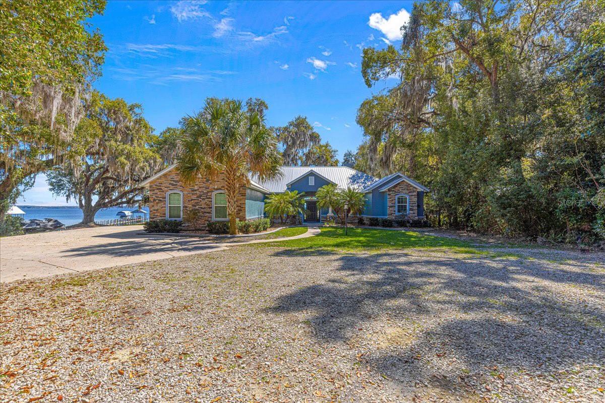 Experience the ultimate in lakefront living with this exceptional waterfront property on Lake Weir, where you can fully embrace the beauty and tranquility of lake life. This stunning, newer construction home, built in 2016, sits on a private 1.91-acre lot with approximately 149 feet of frontage on popular Lake Weir. Lake Weir is a 5,600-acre deep-water lake renowned for its excellent location in Central Florida and superb recreational opportunities, including boating, fishing, and water skiing. The 2,846 SF home offers a perfect blend of luxury and comfort, featuring a side-load, oversized 2-car garage and extended paved areas. Inside, the open-concept design includes a high-end stainless kitchen with a large island, gas cooktop, and under-counter ice maker, flowing seamlessly into the living and dining areas. Vaulted wood ceilings and large windows provide breathtaking views of the water. The glamorous master suite boasts tray ceilings and a luxurious bath with both a soaking tub and a large walk in shower, plus dual vanities and oversized closets. There are two guest rooms, featuring a Jack-and-Jill bath, and a spacious game room with a half bath. The guest rooms and game room are located on the opposite end of the home from the master suite for added privacy and expanded living areas. Sliding glass doors throughout the home open to back terraces and porches, perfect for enjoying the lakefront views. Additional highlights include a propane fireplace, built-ins in the living room, and a private master porch. Outdoors, a fixed wood dock with a covered cabana and boat lift, along with a pristine sandy beach, provide the ideal space for lakefront entertaining. With easy access to shopping, dining, and local amenities, this is the perfect place to enjoy the best of Lake Weir living.