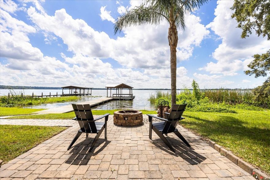 Embrace an elevated lifestyle on the shores of Lake Dora, part of the renowned Harris Chain of Lakes, with this remarkable property featuring a 3-bedroom, 3.5-bathroom main residence and a 1-bedroom, 1.5-bath guest house, a pool, and boathouse—an ideal blend of comfort, function, and lakeside charm. Located just minutes from downtown Mount Dora, this lakeside paradise boasts approximately 80 feet of lake frontage and water access to over 75,000 acres of interconnected lakes, perfect for fishing, cruising, or waterfront dining. The main home welcomes with a bright, open layout where the kitchen, living, and dining areas flow seamlessly—each thoughtfully designed to maximize lake views. The kitchen showcases granite counters, a generous island, and premium cabinetry, all anchored by modern appliances. The living room centers around a gas fireplace flanked by built-in shelving and transom windows that usher in natural light. The first-floor primary suite is a peaceful retreat, complete with dual walk-in closets and a uniquely designed bath layout: two private half-baths connected by a shared walk-in shower—an intelligent configuration that provides both privacy and convenience. Upstairs, an additional bedroom, full bath, and a spacious loft provide flexible space for guests or a home office. The guest house mirrors the quality and care of the main home, with a full kitchen, ADA-accessible en-suite bedroom, and its own laundry area—perfect for multi-generational living or long-term guests. Outdoors, enjoy Florida living at its finest: a heated, saltwater SwimSpa pool with in-water treadmill, screened lanai with grilling hookup, pavered firepit area, and a solar-powered boathouse with a lift for your 23-ft Tritoon. The oversized lot also accommodates RV or boat parking, complete with a 30-amp outlet. Practical upgrades include a whole-house generator, EV charging, and a newly installed HVAC system (2024). With direct lakefront access, thoughtful enhancements throughout, and unbeatable proximity to downtown Mount Dora’s shops, restaurants, and year-round festivals, this is a rare opportunity to enjoy both relaxed everyday comfort and a quintessential Central Florida lifestyle. See this exceptional property for yourself; schedule your private tour today.