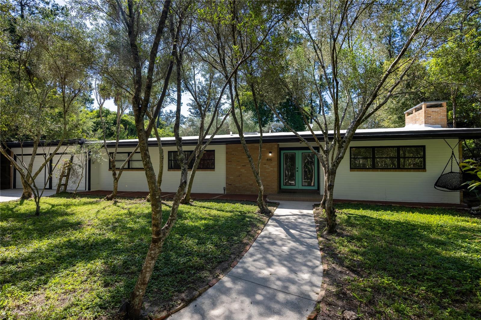 For sale in Black Acres, an amazing Mid-Century Modern brick pool home complete with tree house. This 4 bedroom plus flex space, 3 bathroom home was built in 1959 and is blocks from the University of Florida Law School. Located on nearly a half an acre lot, this 2,984 heated and cooled home has all the charm yet has been thoughtfully updated. Period finishes include gorgeous terrazzo floors with unique decorative designs, vaulted wood beam ceilings, brick construction and vintage tiled bathrooms. Located in NW Gainesville, Black Acres is a quiet tree lined community within walking distance of Loblolly Woods Nature Park, Westside Park and Hogtown Creek. Just a few blocks away is a Publix Shopping Center with area shops and restaurants. Updates include new Kitchen in 2010, new windows, tankless gas water heater in 2015, water supply lines replumbed, HVAC 2010, mini-splits in 2022 and recoated roof in 2025. From the circular drive, you enter through a grove of olive trees and cactus that offer beauty and privacy from the street. On the front porch you will love the double front door that allows a ton of natural light into the foyer. The terrazzo, found throughout the entire home, is in amazing condition. The change of color and decorative designs offer a fun play on light as you move from area to area. To the right of the Foyer is the large Living Room with wood beam vaulted ceiling, wood burning fireplace with stone hearth and vintage tile and built-in wood cabinets. The space flows seamlessly into the brick-walled Florida Room overlooking the rear garden and screened, in-ground pool. To the left of the Florida Room is the large open Family Room. There is a breakfast bar that opens to the Kitchen. At the end of the Family Room is a second fireplace and wood oven. To the right is a storage closet and to the left the room opens to the Kitchen and Dining Area. The Kitchen has stainless steel appliances, double electric oven, gas range, microwave, skylight and granite counter tops. The Dining Area is open, has the wood beam vaulted ceiling, storage closet and solar tube. To the right of the Dining Area is access to the In-Law Suite and Laundry closet. The laundry area includes a washer and gas dryer. The In-Law Suite has a large bedroom with built-in bookshelves, separate entrance, access to the garage and private patio and covered, screened porch, through the bedroom you enter the flex space. There is a full kitchen and en suite bathroom. This flex space could be the living room of the In-Law Suite, additional sleeping space, office or studio. It has a second, separate entrance as well. The screened porch off the flex space overlooks a decorative creek bed with lush tropical foliage. Enjoy the view from the porch or outdoor soaking tub. To the left of the dining area are two guest bedrooms that share a guest bathroom. One bedroom has a vaulted ceiling and built-ins. The other overlooks the front yard and is full of natural light. The guest bathroom has a tub/shower and has been impeccably maintained. To the left of the foyer is the Primary Bedroom with built-in dresser, two large closets and en suite bathroom. The large room has a vaulted ceiling and double window. The vintage bathroom is in beautiful shape with a large vanity and shower/tub. Two car garage. Partially fenced rear yard. The side yard includes a two story treehouse. The yard includes citrus, persimmon, fig, blueberry and grapes. Zoned for Parker Elem, Westwood Middle and GHS.