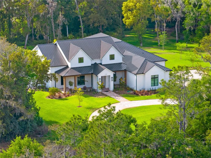 Truly extraordinary modern farmhouse estate on nearly two acres of land in the exclusive Liberty Oaks gated enclave community. The grand double-door entrance opens to the expansive floor plan consisting of an abundance of living spaces, including a true great room, large bedrooms, two offices and a vast flex room currently being used as a fitness area, all surrounding a custom pool oasis and detached guesthouse. Every detail is intentional, from the vaulted 12-foot ceilings, wood beams, stunning 10-inch wide-plank engineered hardwood floor and striking tile work throughout, stylish feature walls, luxury plumbing and lighting fixtures. The exceptional chef’s kitchen features an oversized island, beautiful cabinetry in different shades, hidden Thermador side-by-side refrigerator and an exquisite LaCornue CornuFe Range with five gas burners and two convection ovens. Additionally, a hidden butler’s kitchen boasts a secondary farm sink, refrigerator, dishwasher and spacious built-out pantry. Adjacent to the kitchen are two additional rooms in a designated wet bar with additional dark cabinetry, open shelving and built-in Miele coffee system, plus a large mudroom filled with gray cabinetry, distinctive brick flooring, along with bench lockers leading to the garage. The oversized master suite is bright with big windows, including a barn door to the elegant master bath having separate vanities with an enormous shower, soaking tub and built-out dream closet. Large impact sliding glass doors lead out to the stunning backyard retreat containing a picturesque, heated saltwater pool and spa, covered outdoor kitchen and outdoor living space, and an open turf lounge area leading to a very generous backyard with wooded views. Connected to the pool deck is the 842-square-foot detached guesthouse boasting its own bedroom, bath, living room and full kitchen. Key features include split three-car garage, scenic covered front porch area, metal roof, top-of-the-line water filtration system, Generac prewiring, security camera system, tankless water heaters and long circular driveway. The luxury nine-home community of Liberty Oaks includes other new homes of consistent size and style while centrally located just north of Downtown Tampa, near numerous options for dining, shopping, hospitals and highway access to Tampa International Airport.