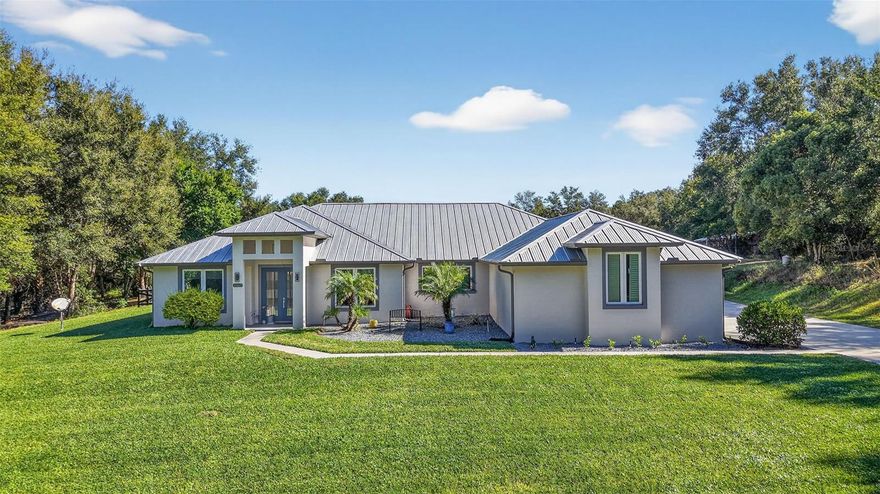 Enjoy peace, privacy and open space the minute you turn down the tree-lined driveway in this custom-built 2018 home. Situated on 5.8 acres just minutes from historic Downtown Mount Dora, this modern house has been thoughtfully designed for indoor-outdoor living with an open-concept living and dining room featuring sliders that open out to an expansive lanai. The saltwater pool is completely screened and overlooks the serene pasture, creating the perfect space for entertaining or quiet relaxation. Inside, the kitchen is a beautiful gathering spot with a sprawling cooktop island, quartz countertops, farmhouse sink, built-in appliances and custom cabinetry. The large, oversized windows in every space allow you to soak in the natural beauty and privacy this property affords. Retreat to the primary bedroom with pool views, an electric fireplace and luxurious en-suite bath complete with a walk-in shower, separate vanities and ample walk-in closets. Enjoy easy access to the laundry room directly from the primary suite. The split floor plan provides the two guest bedrooms with privacy, each with their own bathroom. And the dedicated office space is both beautiful and practical with double-door entry and another oversized window. 

When you step outside, you have a fully fenced backyard with premium ProVista St. Augustine sod, fruit trees and quick access to a newly built 40x50 metal building and attached lean-to. Inside the detached metal building, you'll find dedicated storage space for recreational toys, equipment, and livestock supplies. Walk through a set of double doors and you're welcomed by an additional 1,360 air-conditioned square feet of entertaining space. With a 4K projector and 150-inch screen, you can enjoy sports, tv and movies from the luxurious comfort of the custom-built stadium seating recliners. An additional three 65-inch TVs, built-in bar, pool table, darts, putting green and video games means there's no shortage of ways for you and your guests to enjoy the ultimate entertainment haven. When you want a break from all the excitement inside, just step out to the covered porch overlooking an irrigated garden and fenced pasture complete with top-board and no-climb wire — ready for your livestock to call home. Other deliberate additions to the property include a whole-home generator, electric car charging and RV outlet, asphalt driveways and oversized chicken coop. 

While the property is tucked away in a quiet setting on land with no HOA or deed restrictions, it offers both privacy and convenience. Just a mile from downtown Mount Dora and its historic shops and restaurants, and nearby access to Highway 441 and Interstate 429 connects you to Orlando’s business hubs, premier shopping, airport, world-class attractions, and Florida’s beautiful East Coast beaches.